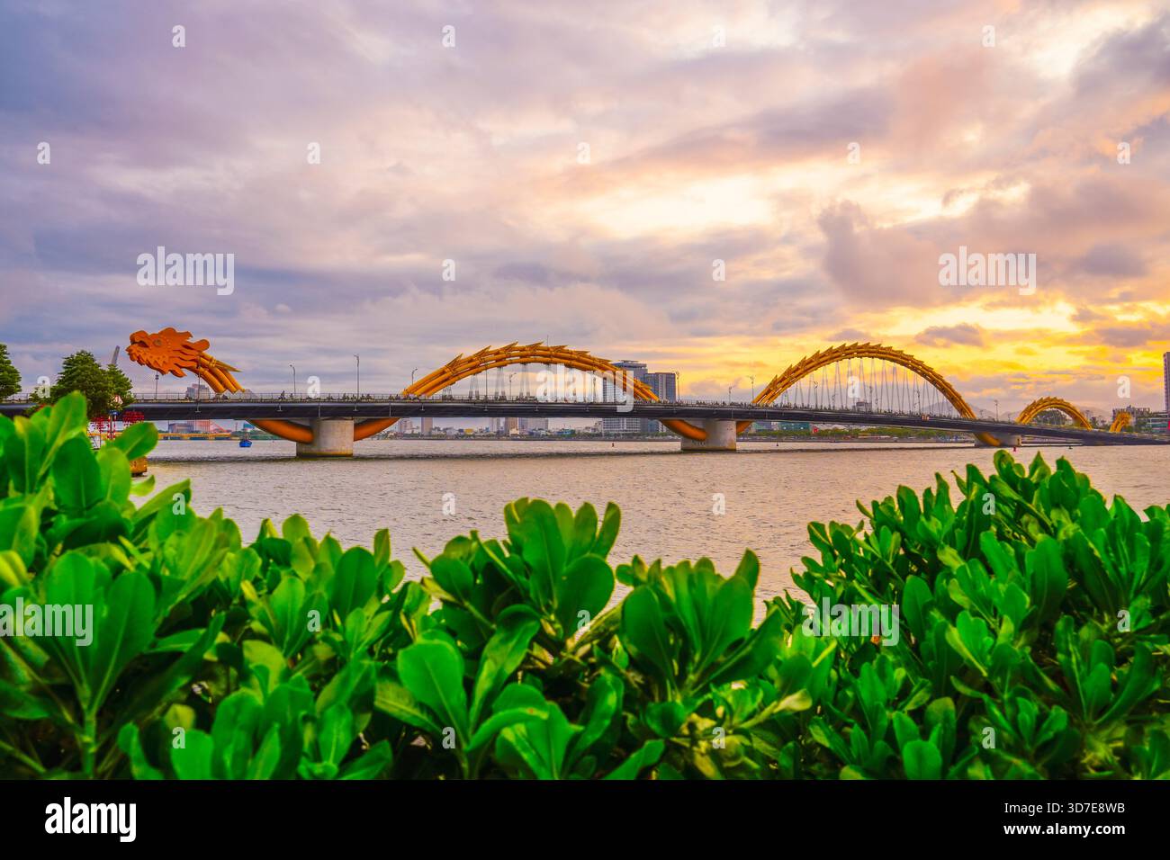 Kopfblick auf die Drachenbrücke bei Sonnenuntergang am Abend in der alten Stunde wunderschöne Wolken mit einem warmen Farbton mit grünem Laub und Sträuchern im Vordergrund. Stockfoto