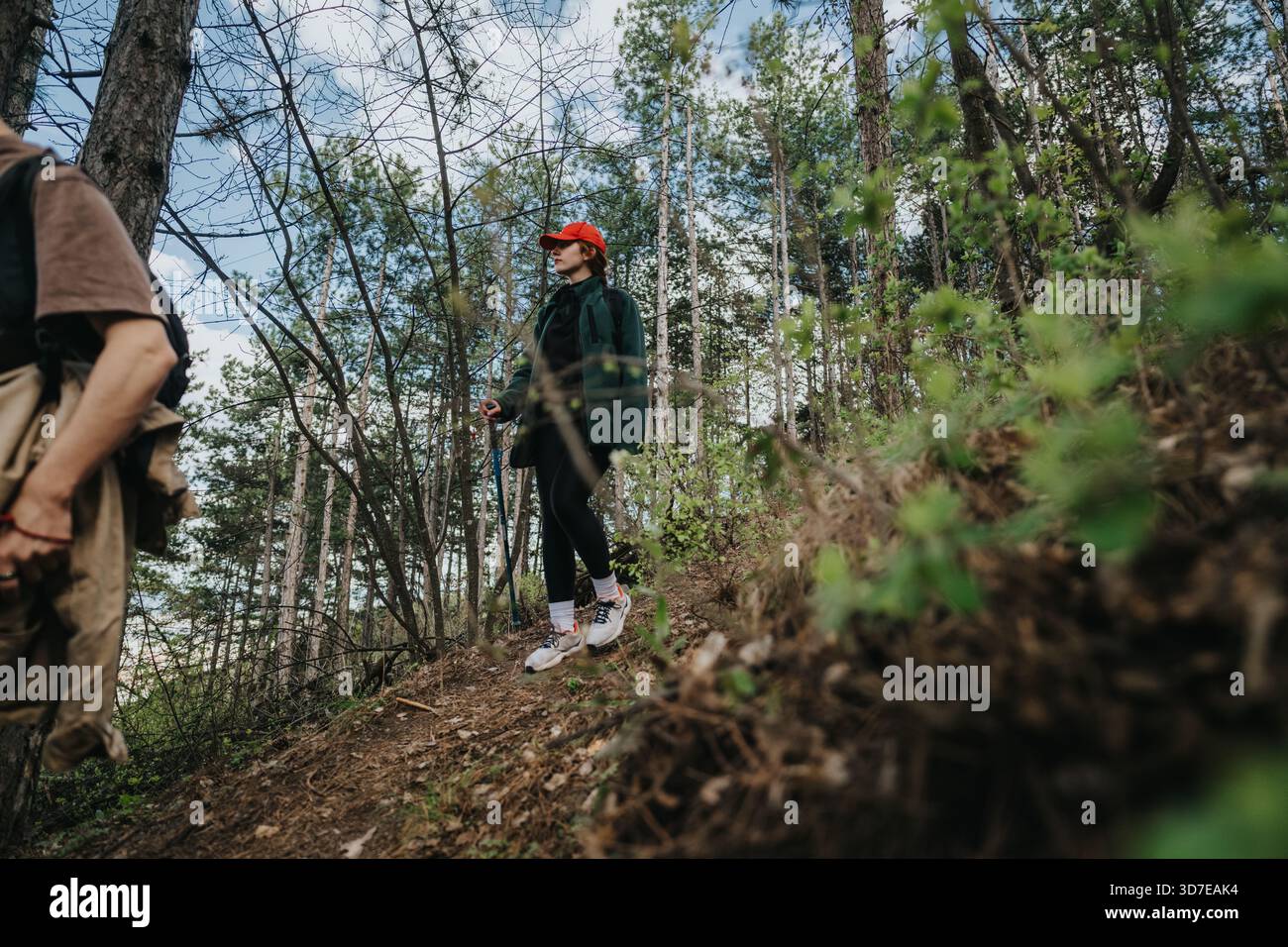 Wanderer auf einem Waldweg mit einer Frau in einer roten Kappe, die einen bewaldeten Hang erkunden Stockfoto