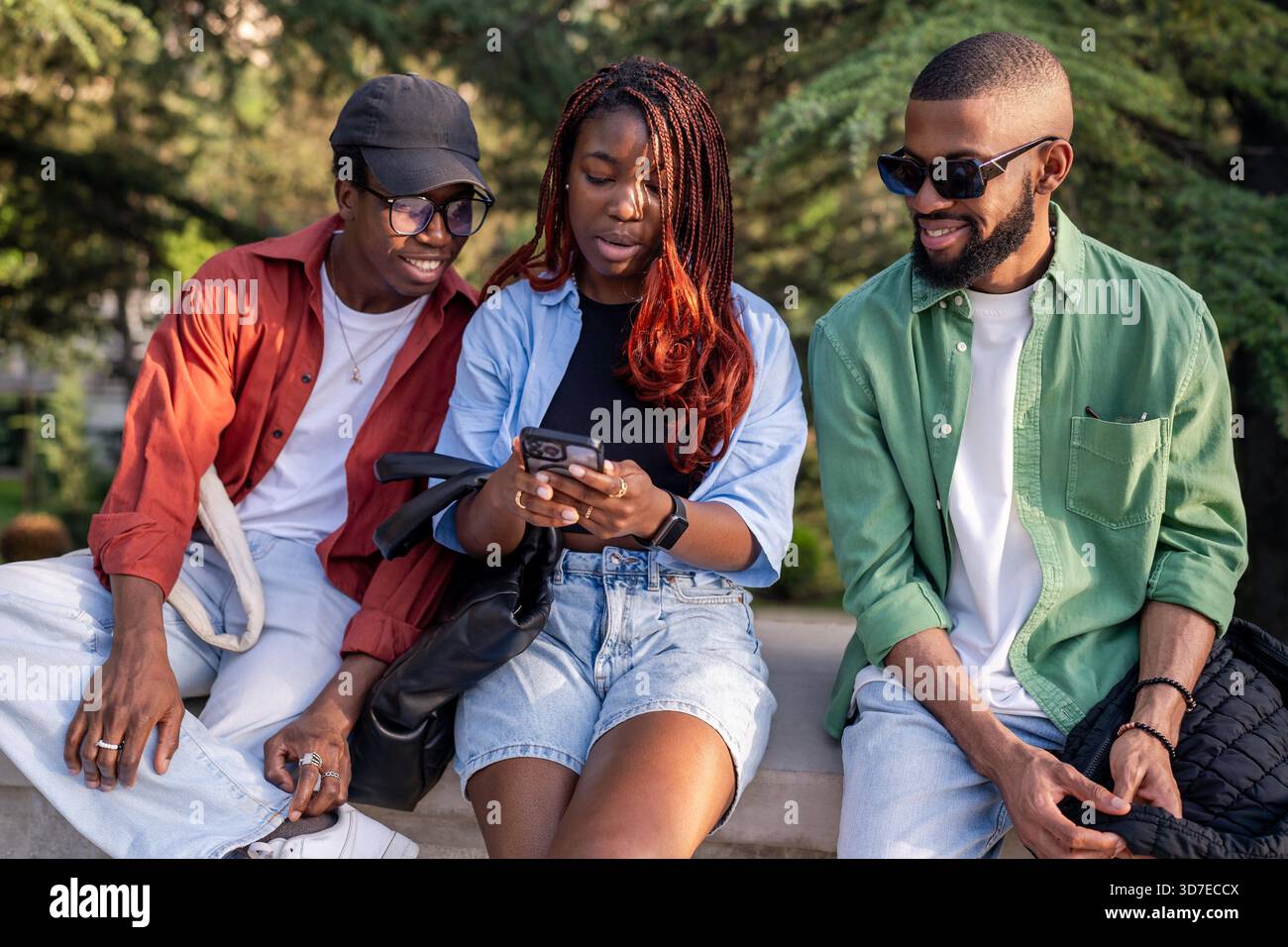 Fröhliche Gruppe afrikanischer Freunde versammelt sich im Park mit Smartphones und teilt Lachen. Black Woman zeigt Post in sozialen Medien, Freunde bewundern Likes, feiern Online-Erfolg, moderne Studenten sind technisch abhängig || Model veröffentlicht Stockfoto
