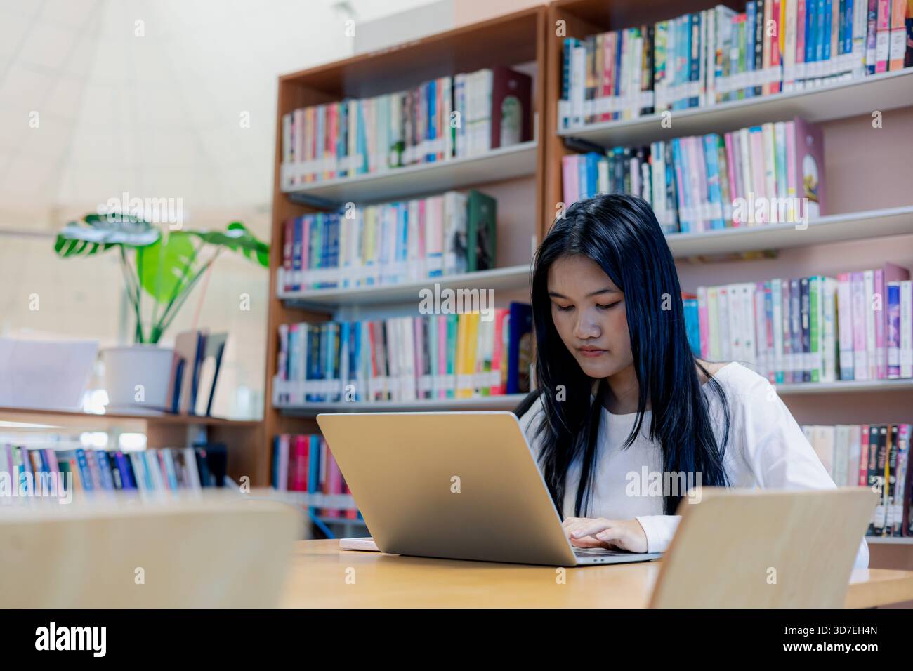 Asiatische Studentin, die Laptop in einer modernen Bibliothek benutzt, konzentriert sich auf das Lernen und Online-Lernen. Bildung, Forschung, Technologie und akademischer Lebensstil Stockfoto