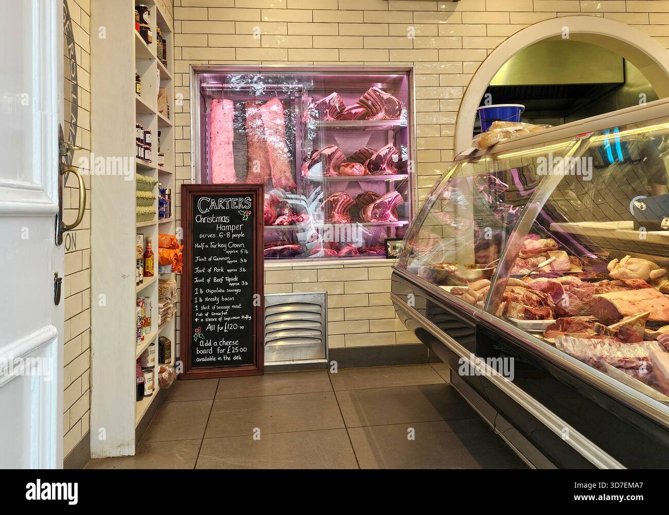 In einer Metzgerei in Bamburgh Village, Northumberland. Große Schnitte in einer Kühlbox und kleinere Fleischsorten in einer Vitrine. Stockfoto