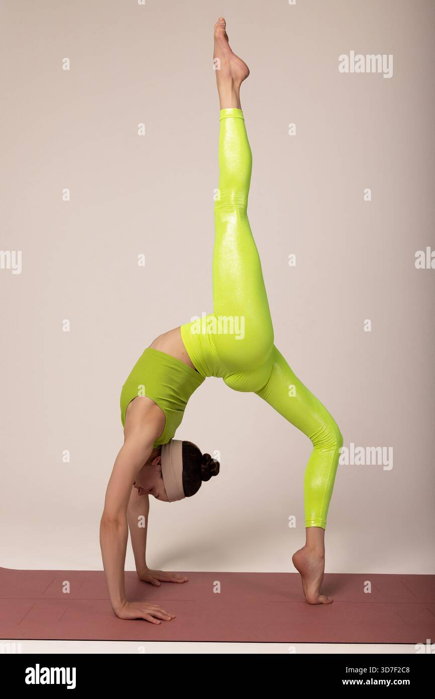 Eine Frau, die eine fortgeschrittene Rückenbeugung mit einem Bein nach oben durchführt, was Flexibilität und Balance zum Ausdruck bringt. Ideal für Fitnesstraining, Yoga-Meisterschaft, AT Stockfoto