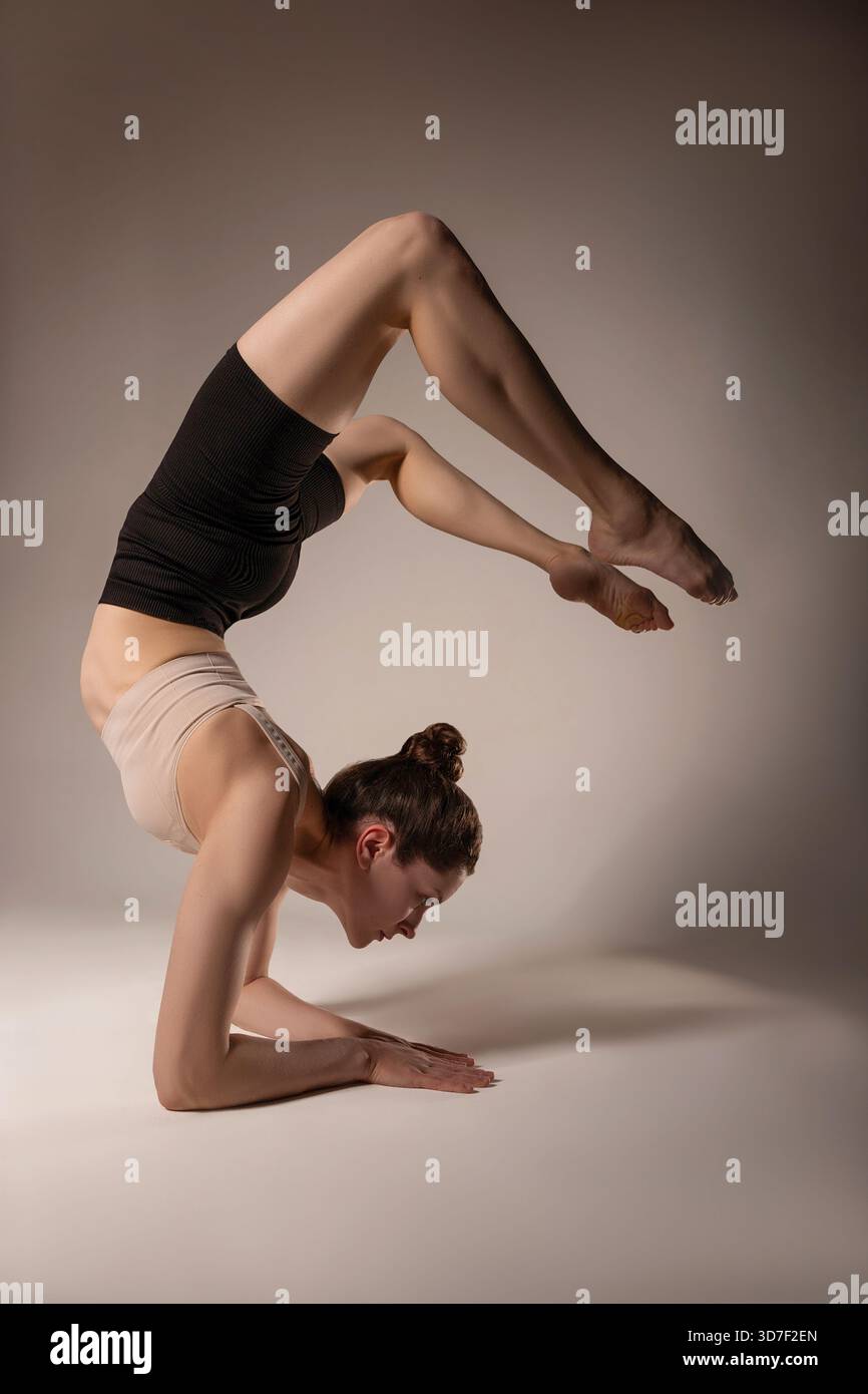 Eine Frau, die einen fortgeschrittenen Unterarmständer mit starker Rückenbeugung ausführt und dabei Balance, Kontrolle und Flexibilität demonstriert. Perfekt für Fitnessmarketing, y Stockfoto