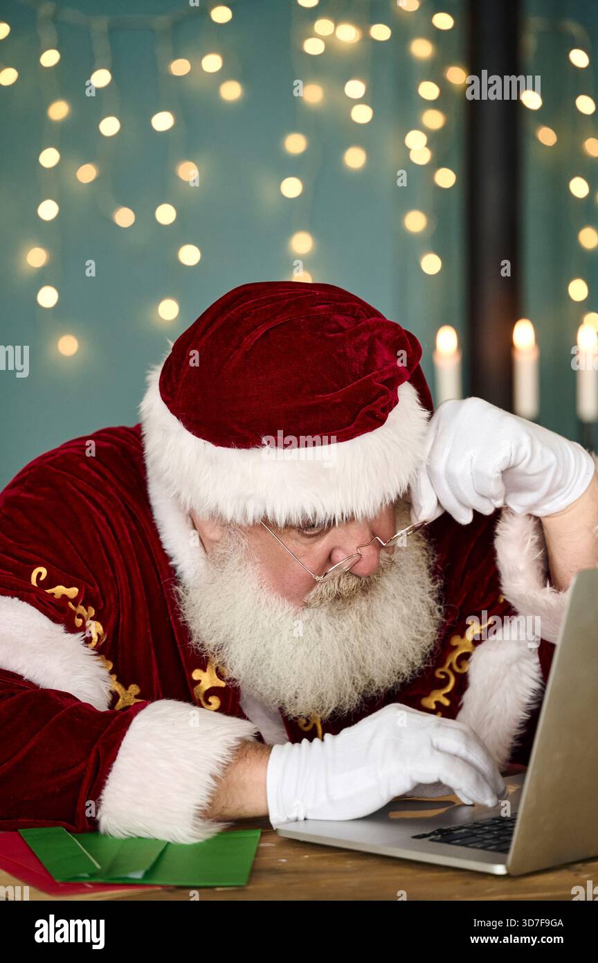 Der Weihnachtsmann liest Kinderbriefe auf dem Computer und bestellt online Stockfoto