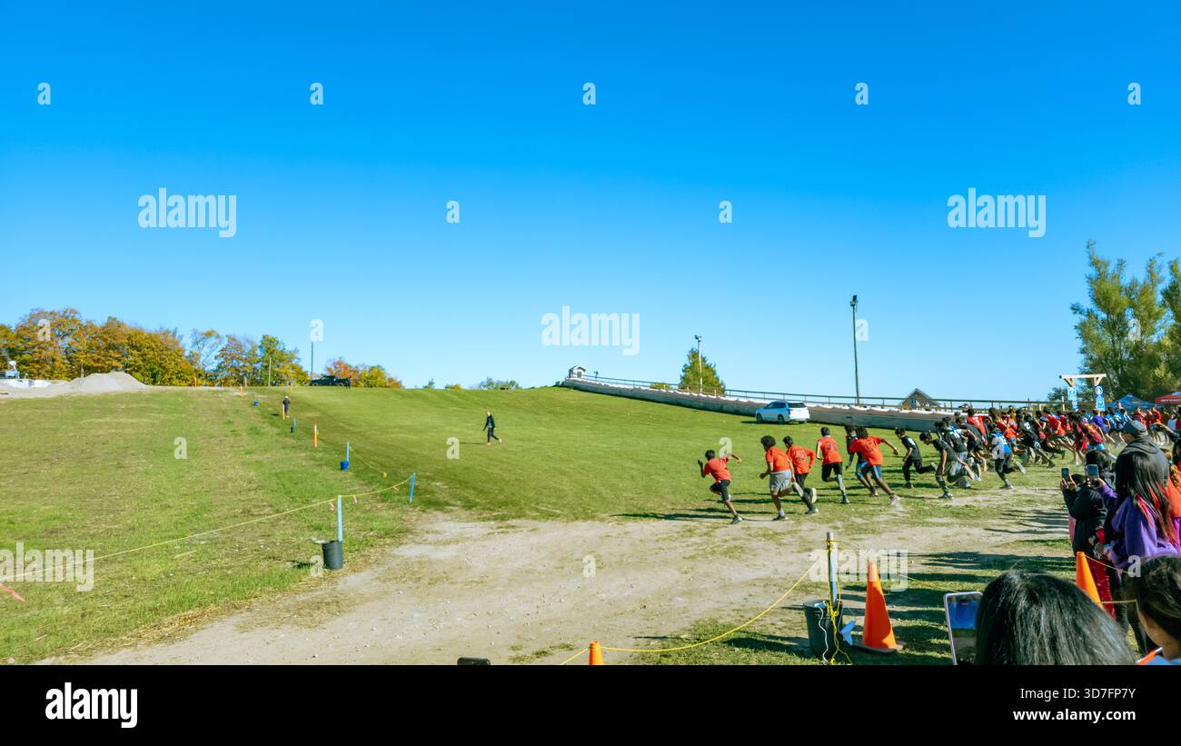 Lakeridge Area in Durham Region, Ontario, Kanada 10-9-2025 Läufer in roten Hemden steigen während eines organisierten Rennens mit Kegeln und Zuschauern auf den grasbewachsenen Hügel - Smartphone-aufgenommenes Stockfoto