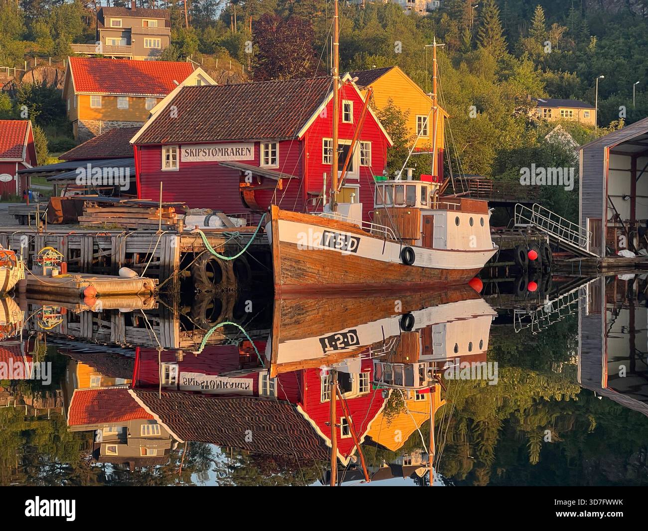 Traditionelles Fischerboot und rotes Bootshaus spiegeln sich im ruhigen Morgenwasser des Hafens von Sagvåg auf der Insel Stord, Norwegen - Smartphone-aufgenommenes Stockfoto