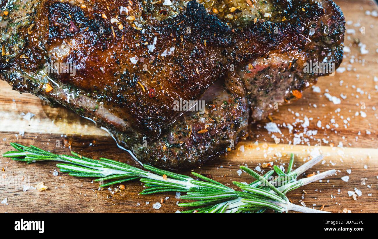 Saftiger ganzer, knochenloser Lammbraten mit Kräutern und Rosmarin auf Holzbrett. Perfekt gewürzt, saftig und bereit zum Schnitzen für besondere Anlässe Stockfoto