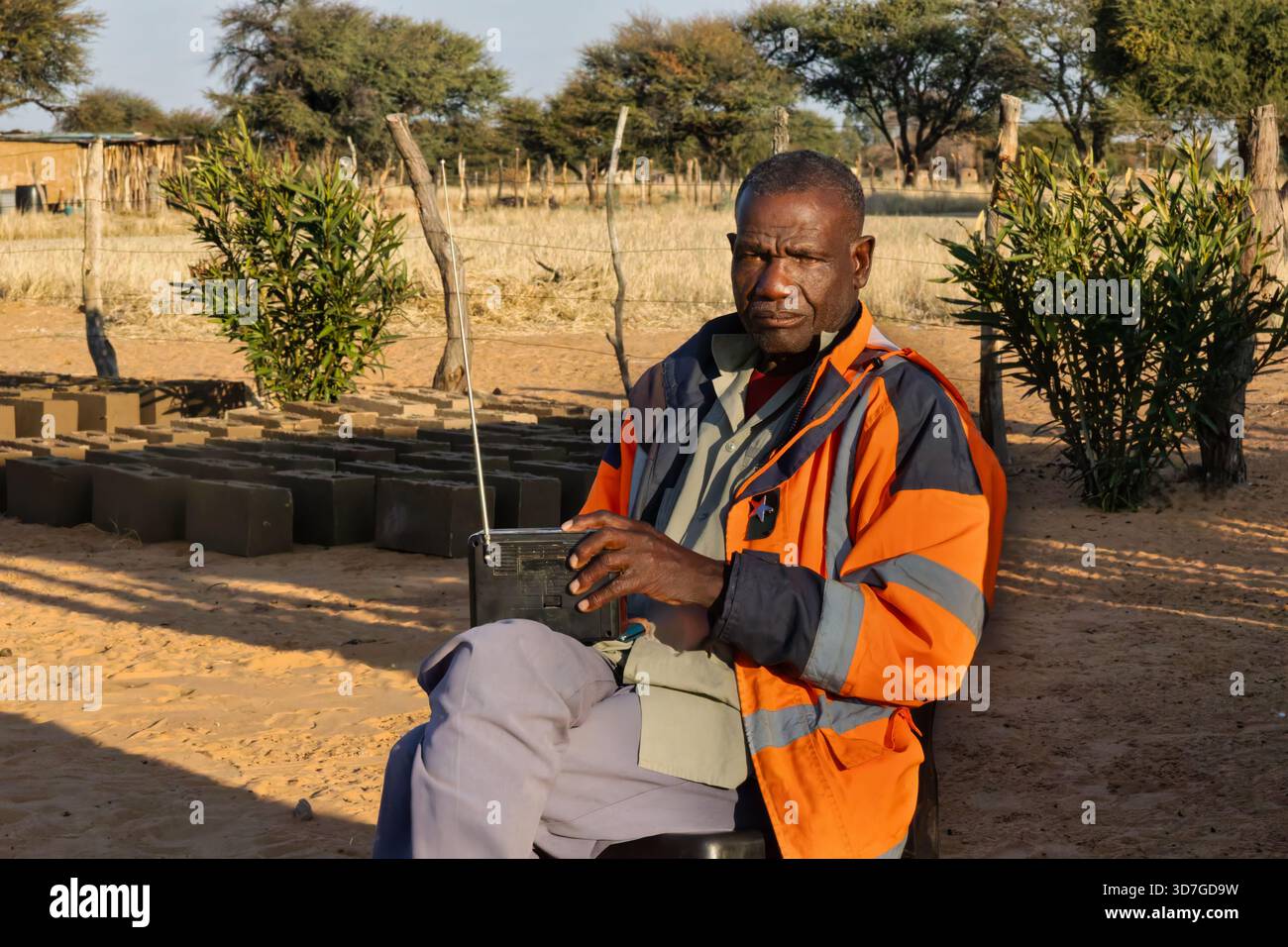 Einzelne alte afrikanische Männer im Dorf, die Radio hören, auf einem Stuhl sitzen, im Hof Stockfoto