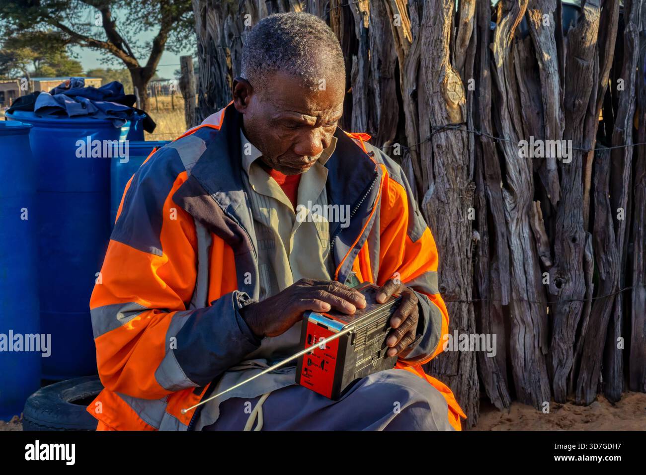Einzelne alte afrikanische Männer im Dorf, die Radio hören, auf einem Stuhl sitzen, im Hof Stockfoto