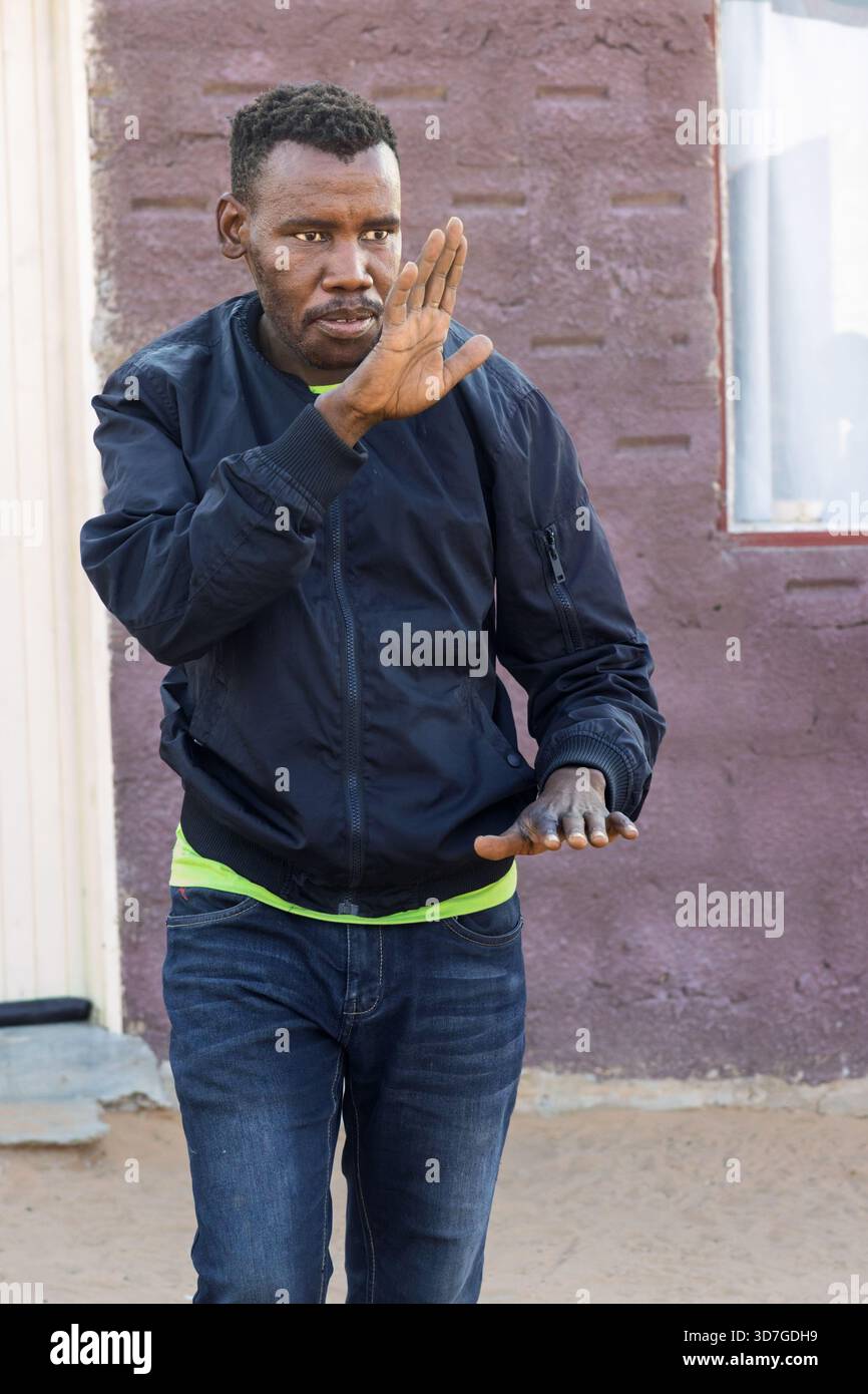 Dorf, einzelne afrikanische Männer grüßen seine Nachbarn, gehen auf dem Hof, vor seinem Haus, im Sand Stockfoto