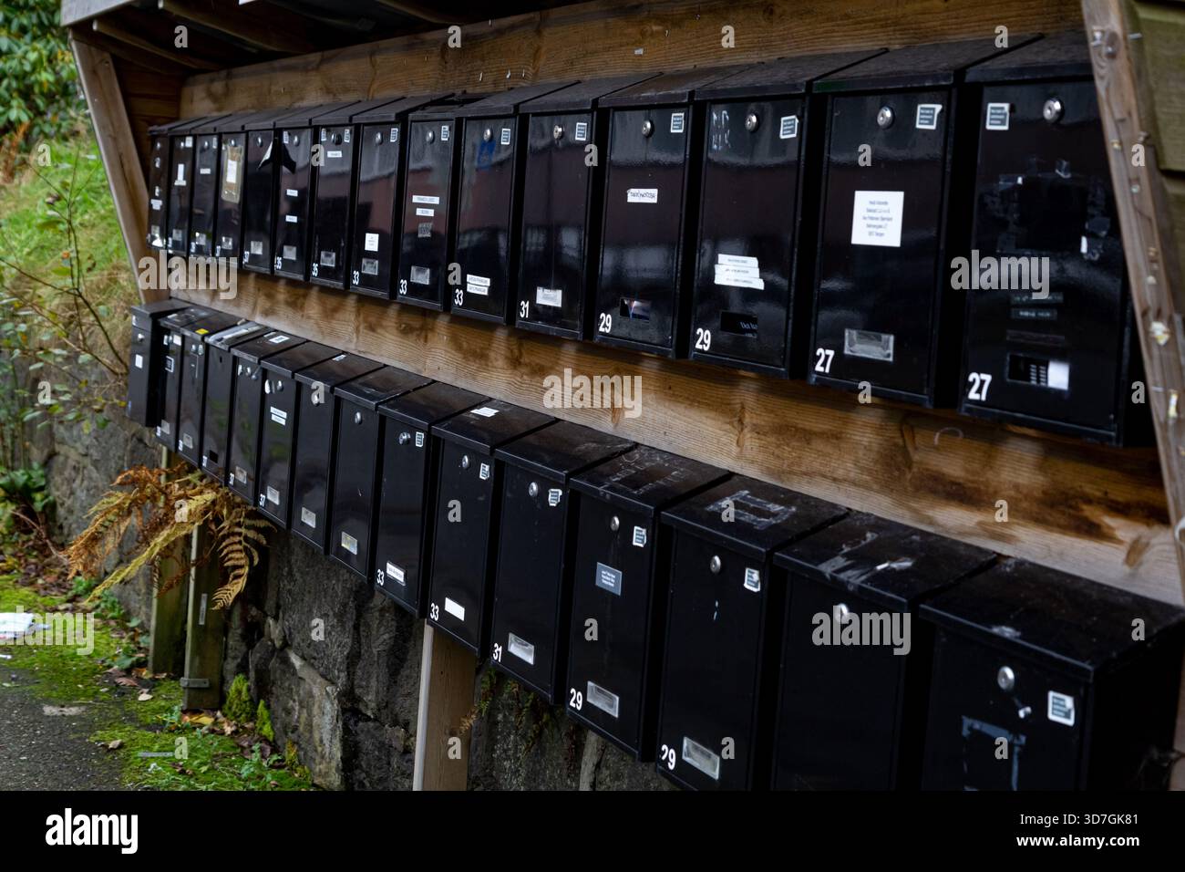 Aus nächster Nähe sehen Sie zwei Reihen schwarzer Briefkästen auf einer Straße in Bergen, die entlang einer Holzwand angeordnet sind. Saubere skandinavische Linien und authentisches nordisches Viertel Stockfoto