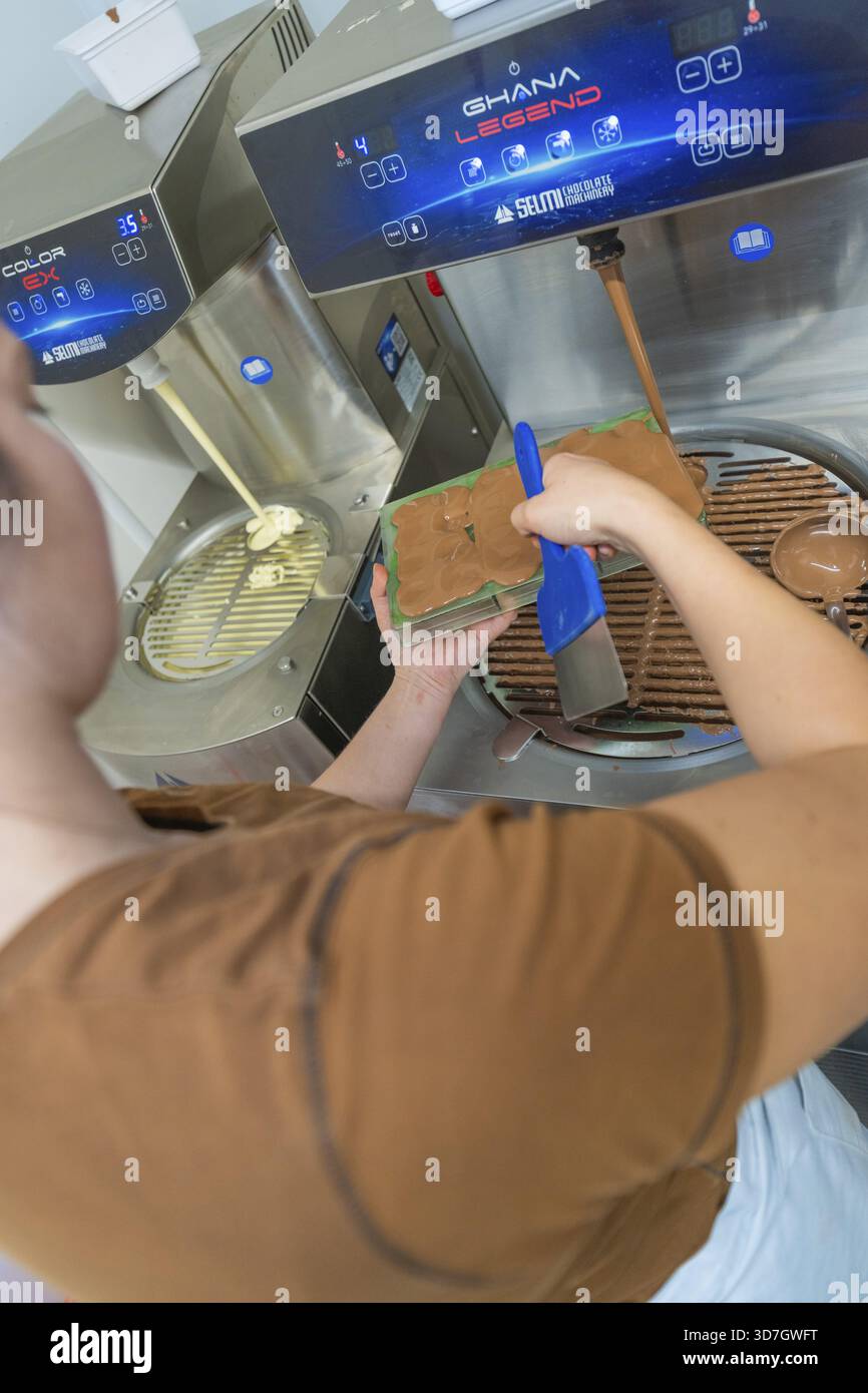 Die Person benutzt ein blaues Werkzeug, um Schokolade in eine Form zu füllen, an einer Tempermaschine, Weihnachtsbäckerei, Haselstaller Hof, Wildberg, Calw District, Deutschland Stockfoto