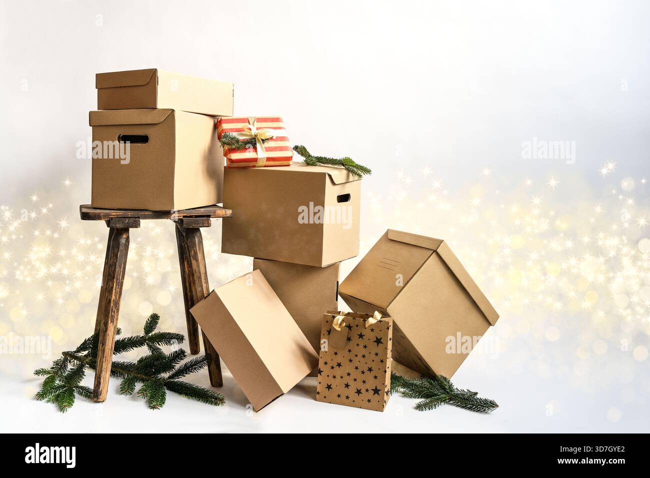 Pappkartons und Pakete in verschiedenen Größen, alter Hocker und Kiefernzweige vor hellem Hintergrund mit Bokeh und Glitzern, Weihnachtsgeschenke, Packagi Stockfoto