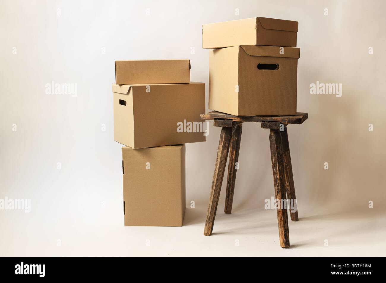 Pappkartons und Pakete auf einem alten Hocker und auf dem Boden in verschiedenen Größen, vor hellbeigem Hintergrund, Konzept für Weihnachtsgeschenke, Packagi Stockfoto