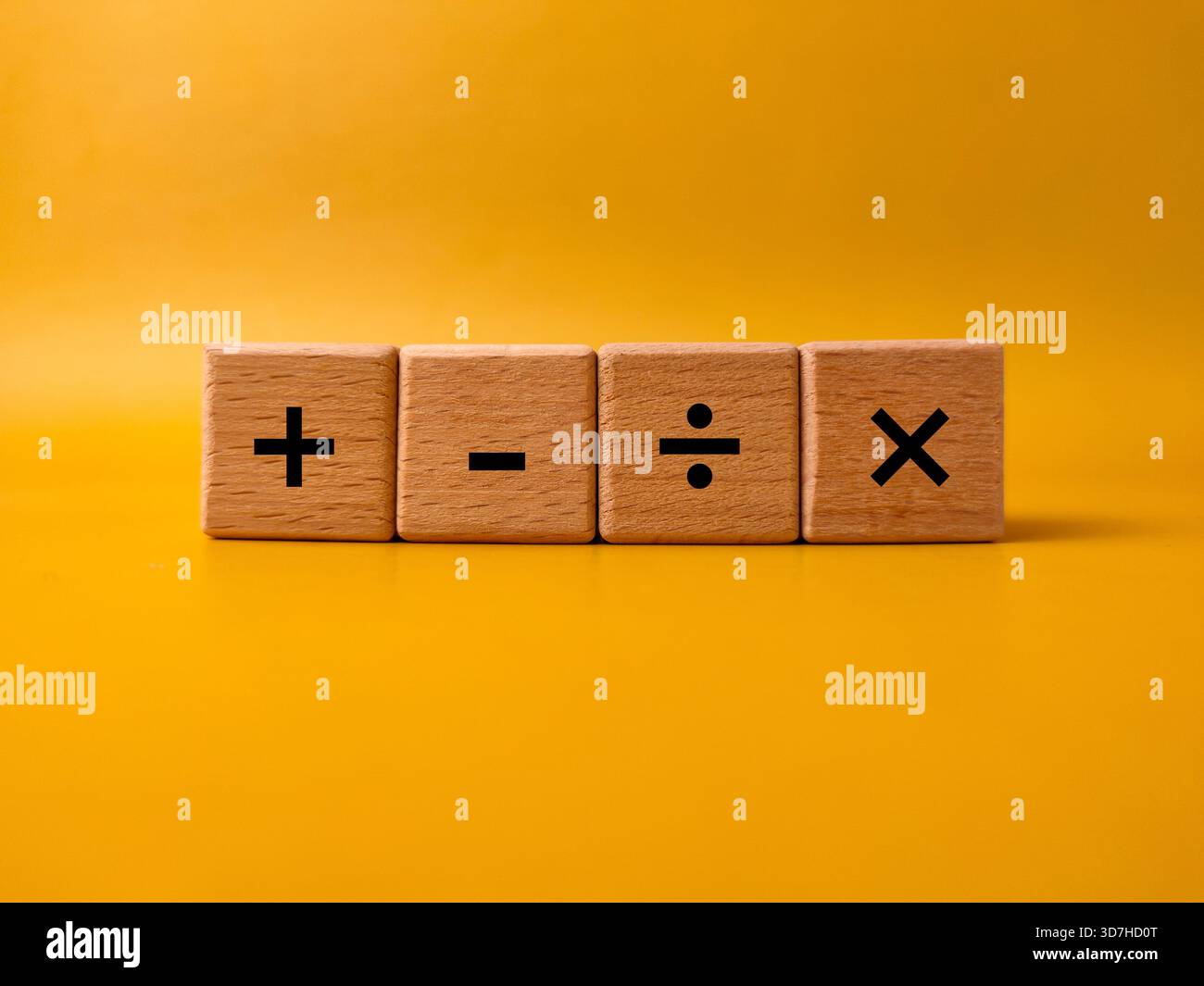 Das Bild zeigt vier Holzblöcke mit grundlegenden mathematischen Betriebssymbolen auf gelbem Hintergrund. Stockfoto