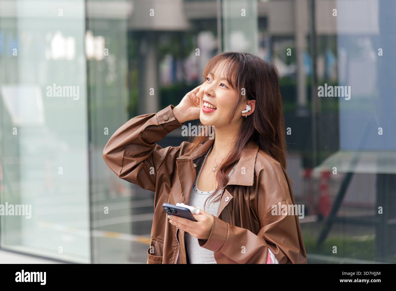 Lächelnde asiatische Frau genießt Shopping-Lifestyle, hält Taschen in der Nähe der City Mall, modisch gekleidet Stockfoto
