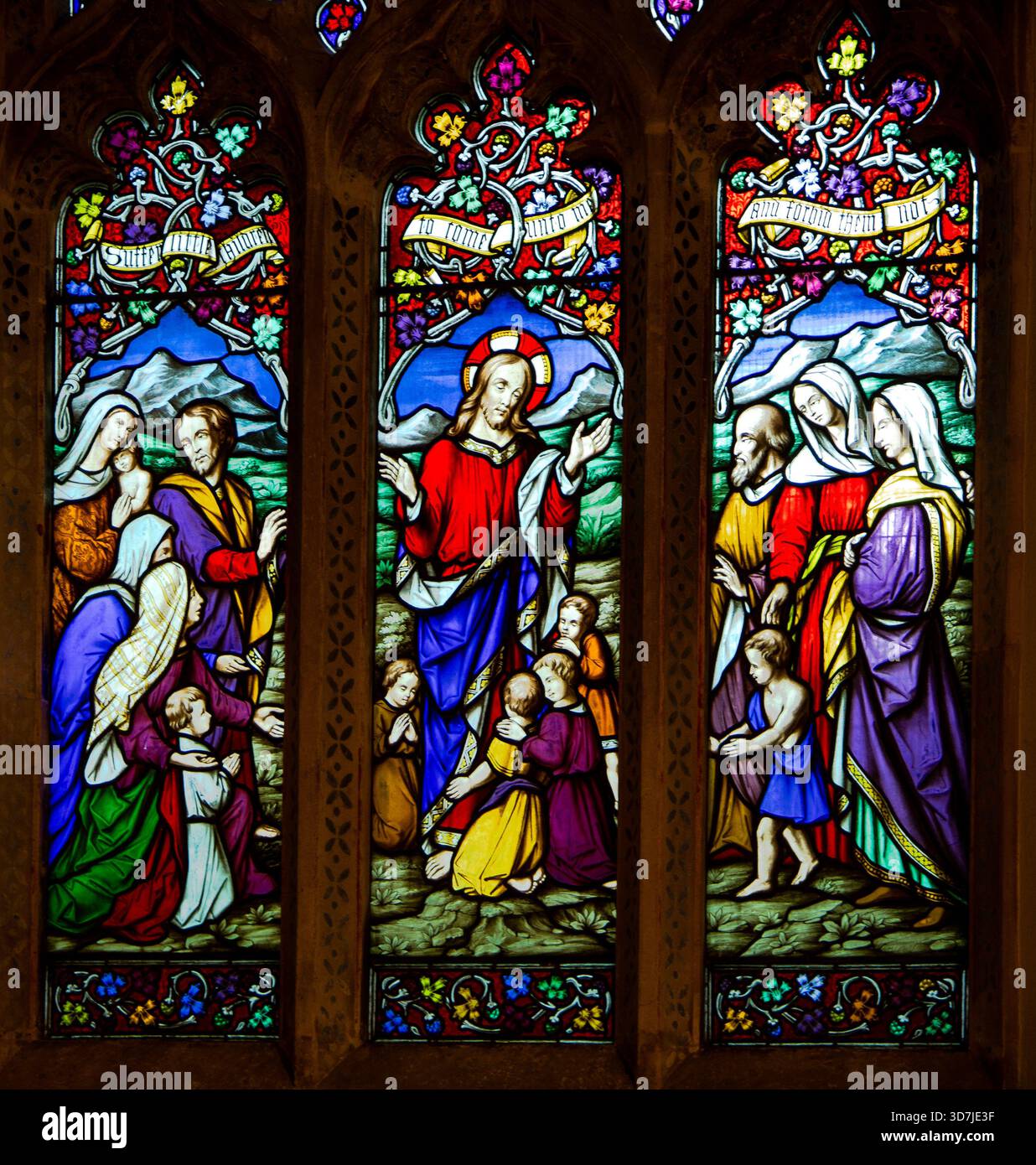Bunte Buntglasfenster, die Jesus mit Kindern und Anhängern in einer traditionellen christlichen Kirche darstellen, St. Andrews Castle Combe UK Stockfoto