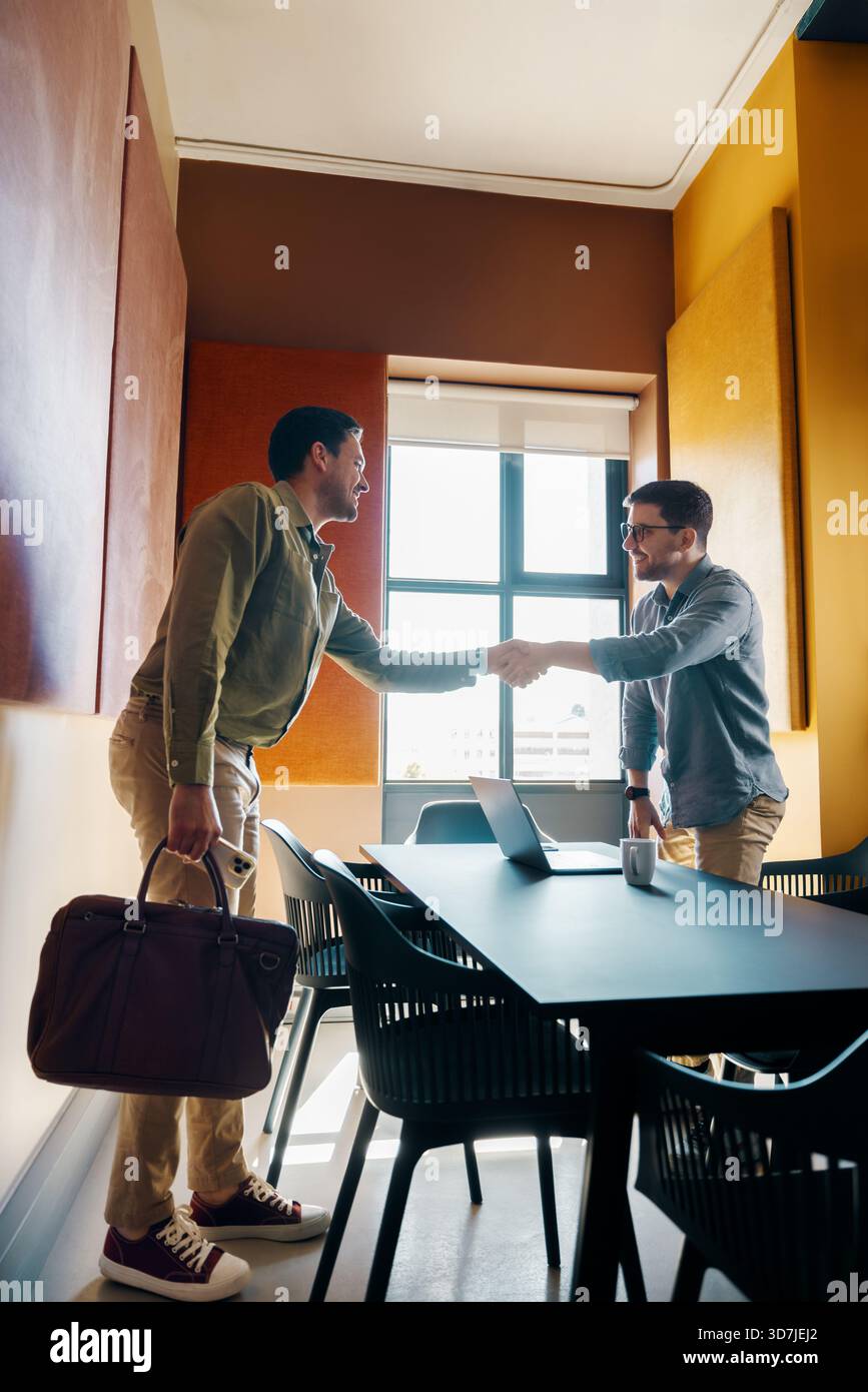 Zwei Männer schütteln sich die Hände in einem modernen Büro. Das Treffen vermittelt Zusammenarbeit und professionelle Vereinbarung unter einer hellen Umgebung mit natürlichem Licht, s Stockfoto