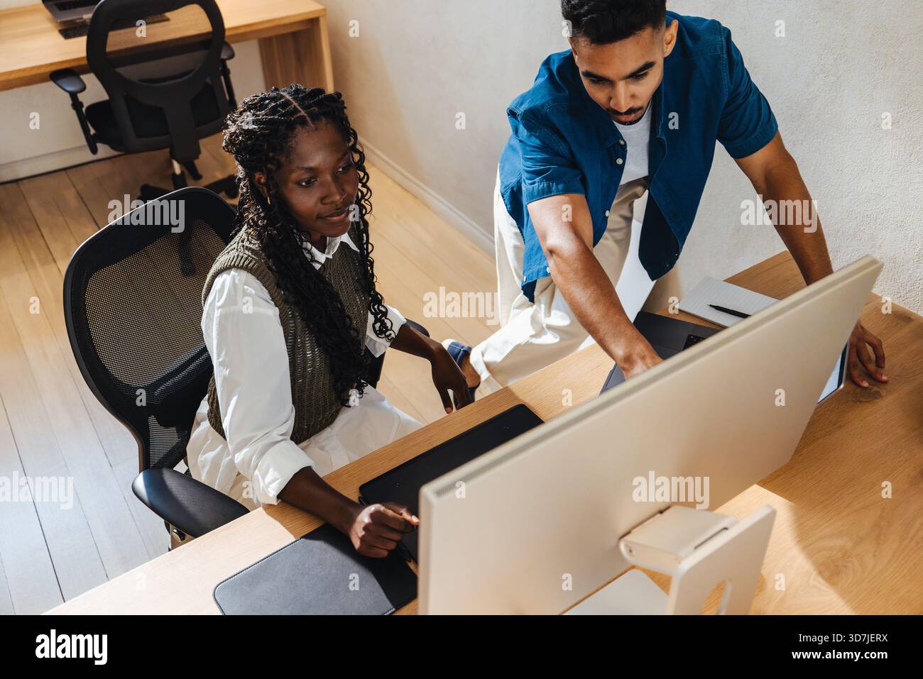 Zwei Kollegen arbeiten gemeinsam an einem Computer in einem aufgeräumten, gut beleuchteten Bürobereich. Sie scheinen fokussiert und engagiert in einem professionellen, kollaborativen s zu sein Stockfoto