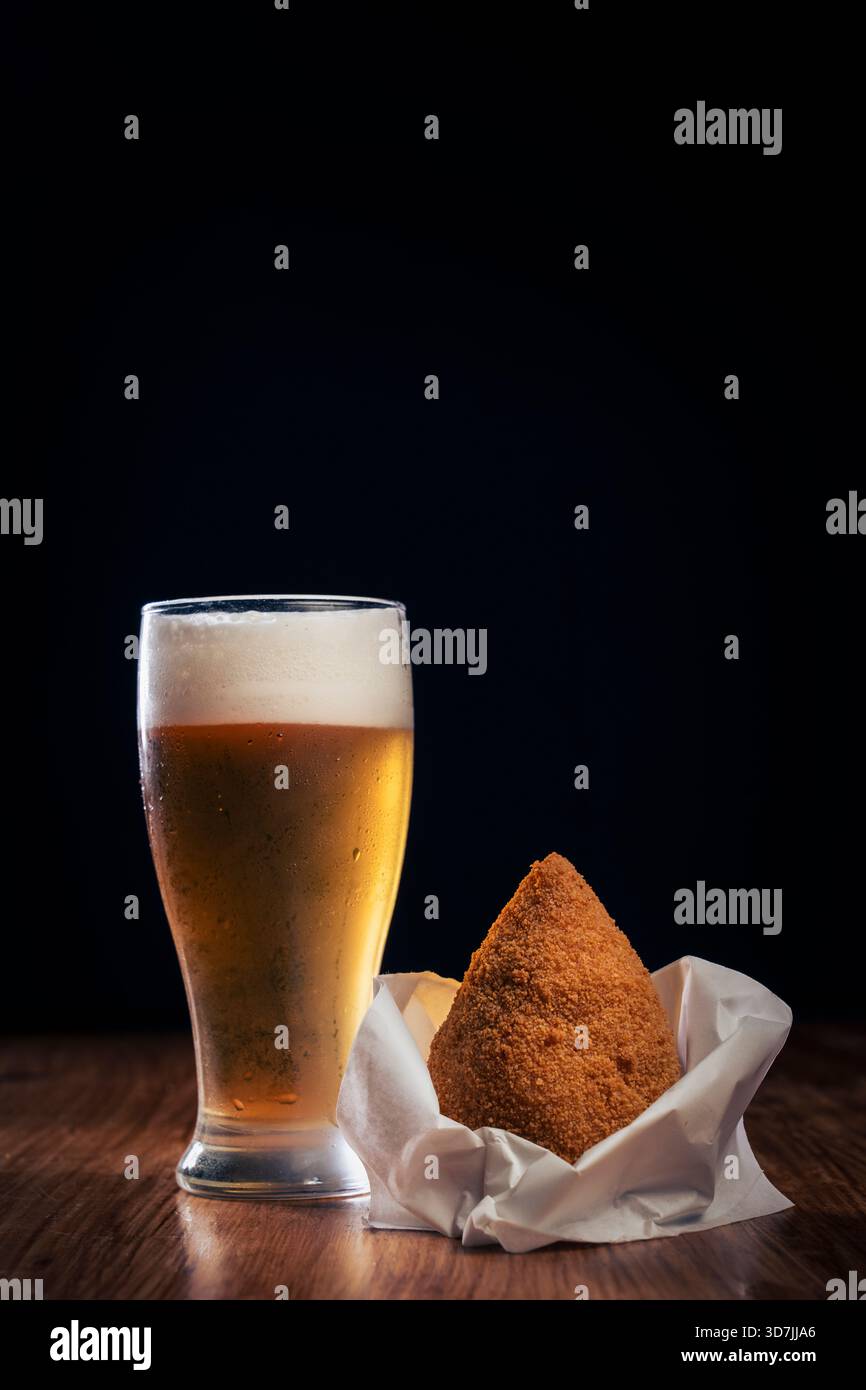 Frisch gebratener sizilianischer Arancino, serviert mit einem Glas kaltem Bier auf einem rustikalen Holztisch. Traditioneller italienischer Reisball-Snack perfekt für Aperitivo Stockfoto