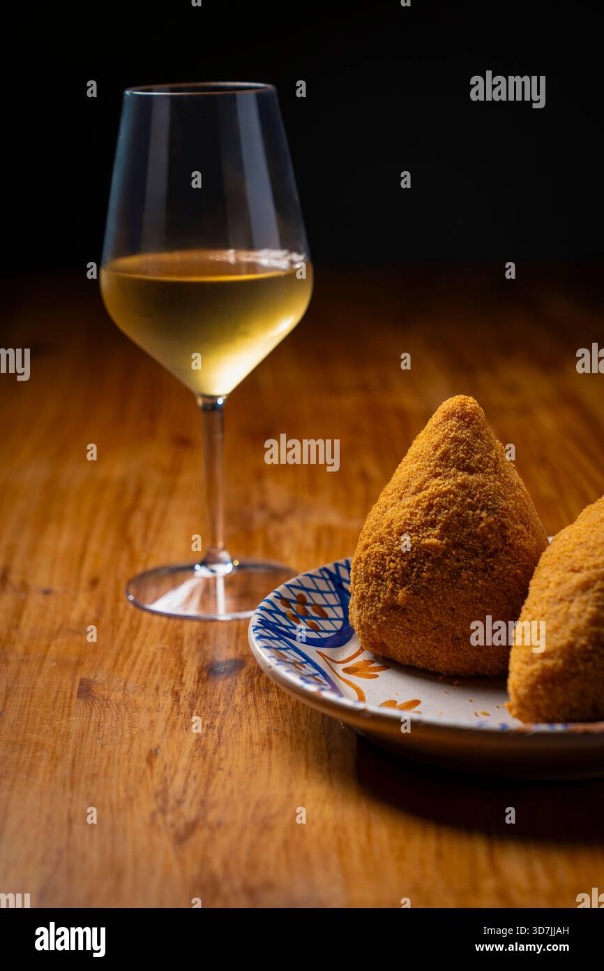 Knuspriges sizilianisches Arancino kombiniert mit einem Glas gekühlten Weißwein. Perfekter italienischer Aperitivo mit gebratenem Reisball und trockenem Wein auf rustikalem Hintergrund. Stockfoto