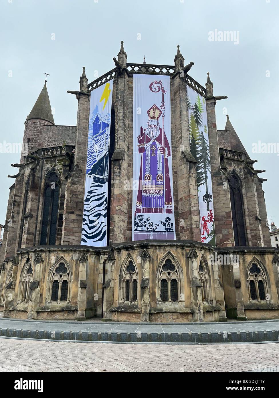 Epinal, Frankreich – 21. Dezember 2024: Mittelalterliche Kirche mit großen festlichen grafischen Bannern, die Wintergeschichten und lokale Folklore illustrieren - Smartphone-aufgenommenes Stockfoto