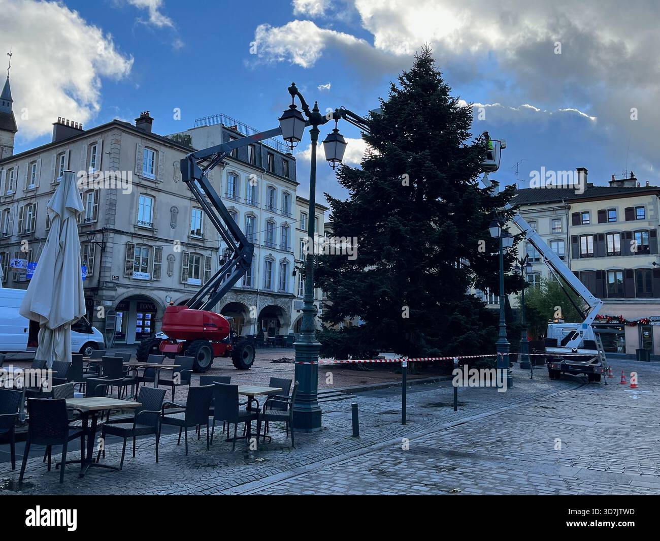Arbeiter verwenden einen Gabelstapler, um einen großen Weihnachtsbaum auf einem Stadtplatz in Epinal, Frankreich, zu installieren und zu dekorieren - Smartphone-aufgenommenes Stockfoto