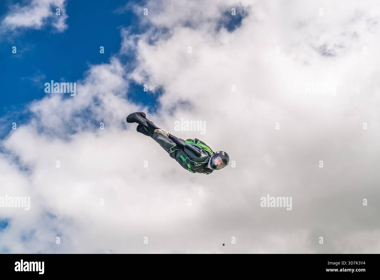 Ein Solo-Fallschirmspringer fliegt fast kopfüber durch den Himmel und behält die aerodynamische Kontrolle während des freien Falls bei Wolken und blauem Himmel Stockfoto