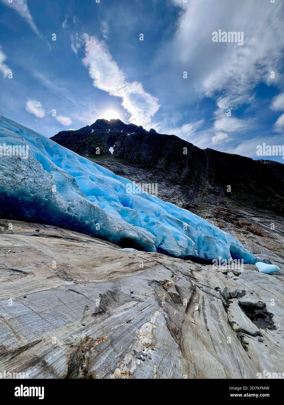 Blaues Eis des Svartisen-Gletschers und quergestreiftes Gestein mit dramatischem Himmel und hinterleuchtetem Bergrücken in Nordland, Nordnorwegen - Smartphone-aufgenommenes Stockfoto