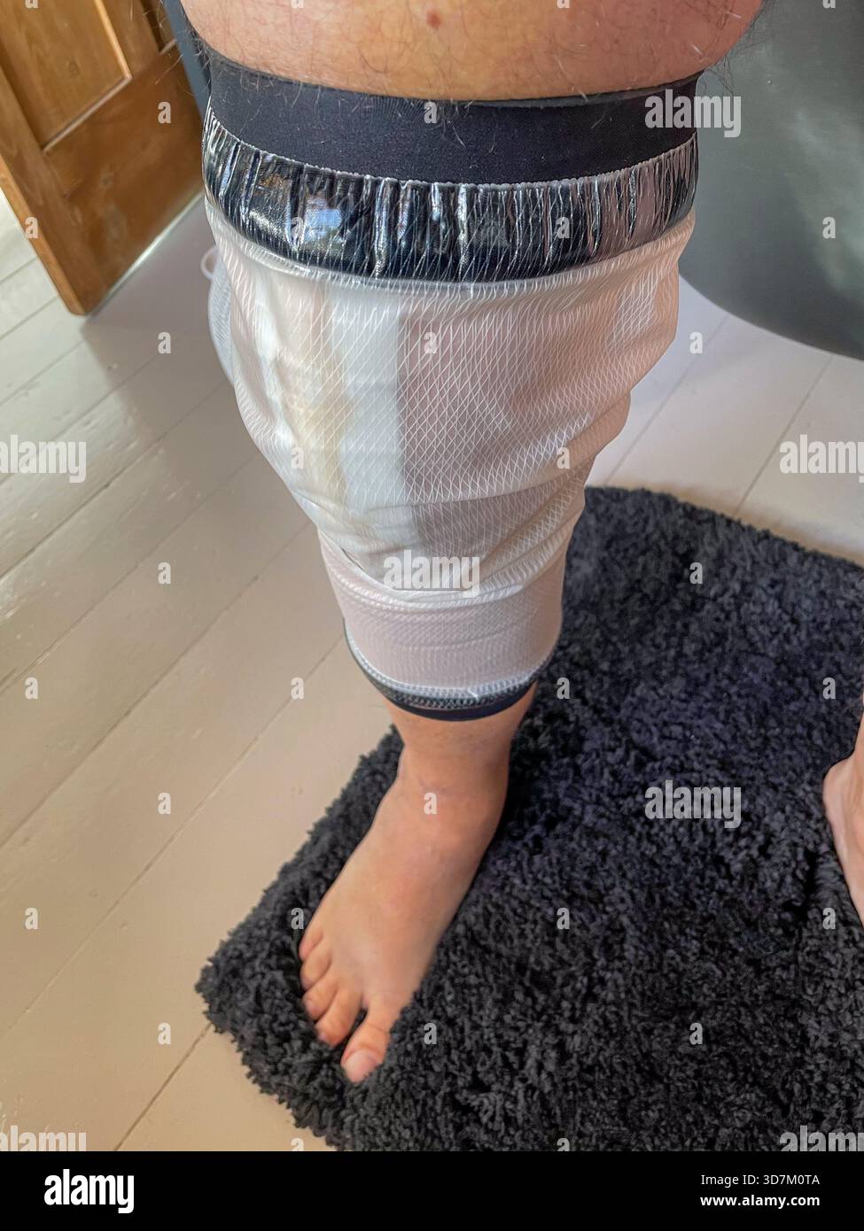 Seniorenmann mit wasserdichtem Beinverbundschutz nach Knieersatzoperationen zu Hause: Phillip Roberts - Smartphone-aufgenommenes Stockfoto
