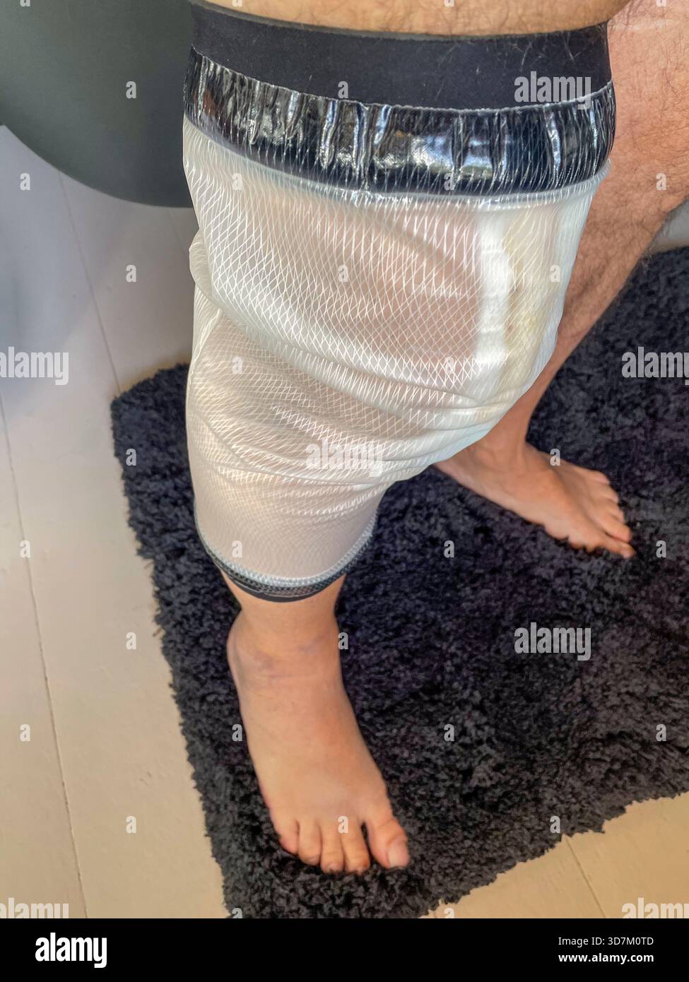 Seniorenmann mit wasserdichtem Beinverbundschutz nach Knieersatzoperationen zu Hause: Phillip Roberts - Smartphone-aufgenommenes Stockfoto