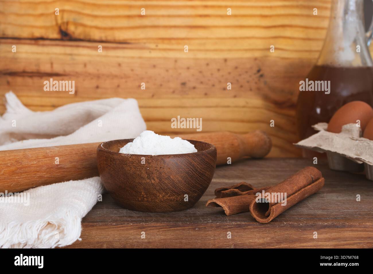 Ein rustikaler Holztisch mit Backzutaten wie Mehl, Zimtstangen, einer Nudelnadel und Eiern für die Zubereitung eines hausgemachten Rezepts. I Stockfoto