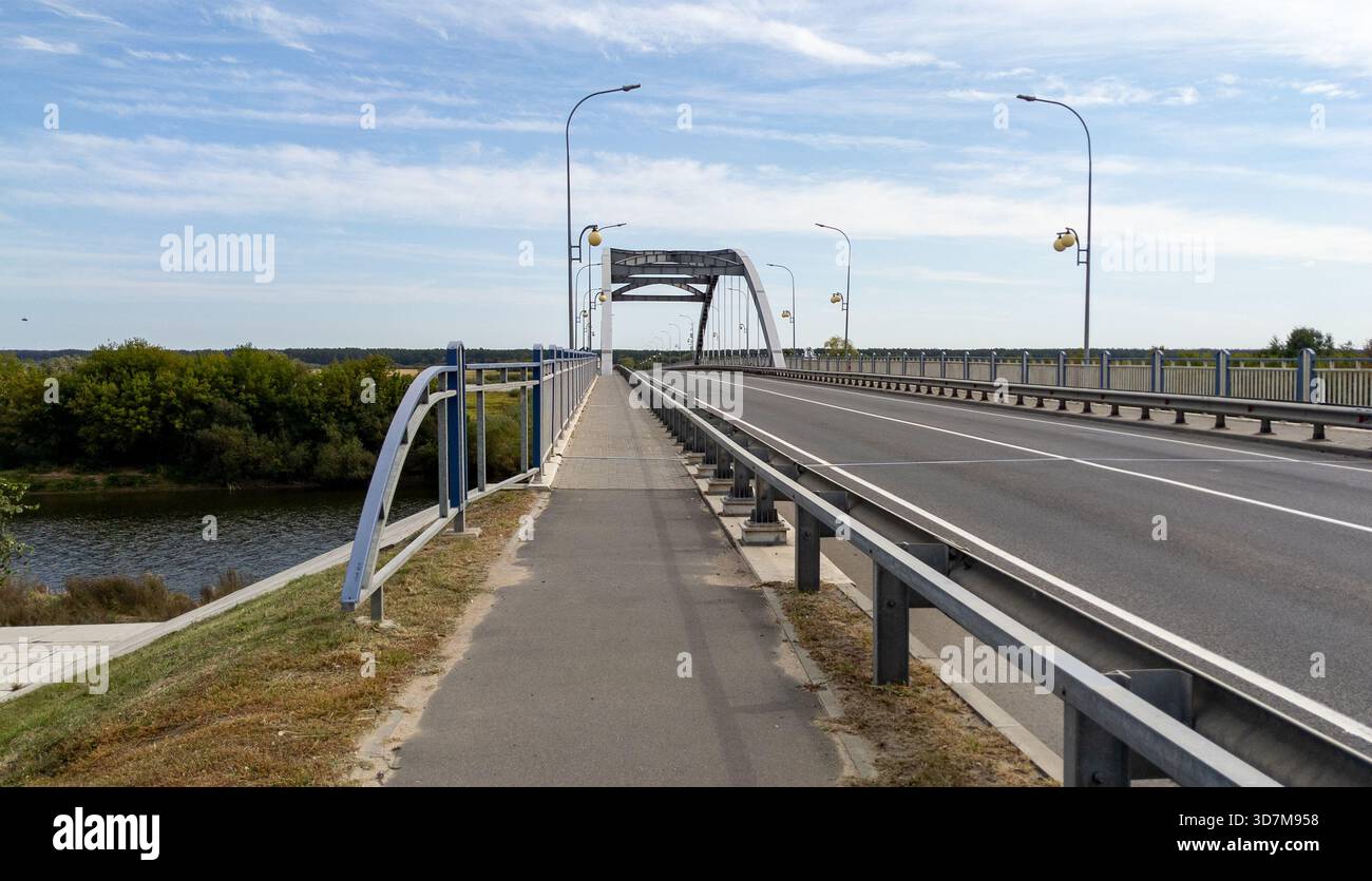 Leere Asphaltstraße auf einer Brücke über einen Fluss an einem bewölkten Sommertag. Blauer Himmel und Wolken darüber. Transportkonzept, Gütertransport, Waren d Stockfoto