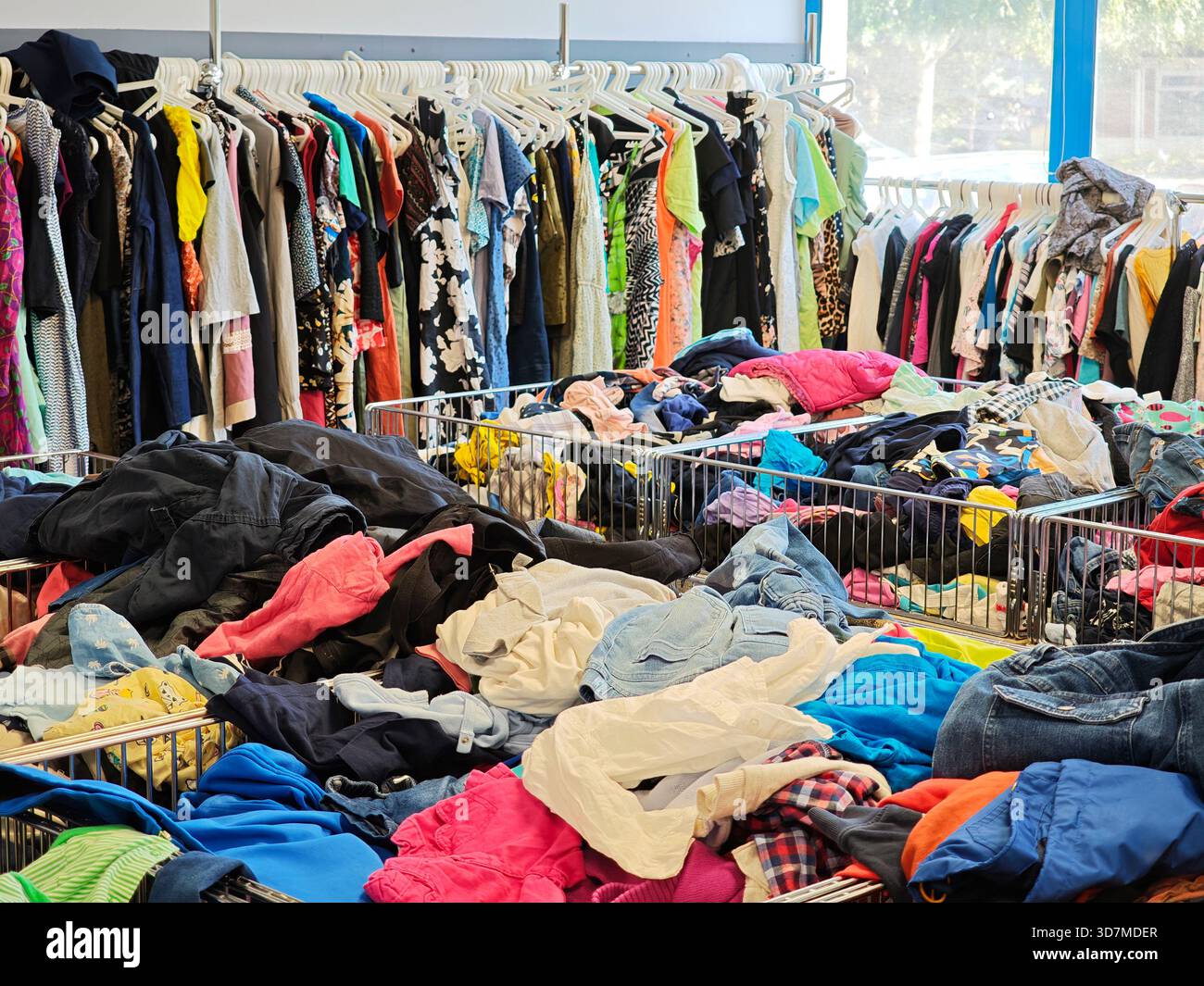 Second-Hand-Bekleidungsgeschäft Innenausstattung mit vielen Haufen gebrauchter Kleidung in Abfalleimern und farbenfrohen Kleidungsstücken, die an Regalen hängen, Aufhängern, die econ-produkte weiterentwickeln Stockfoto
