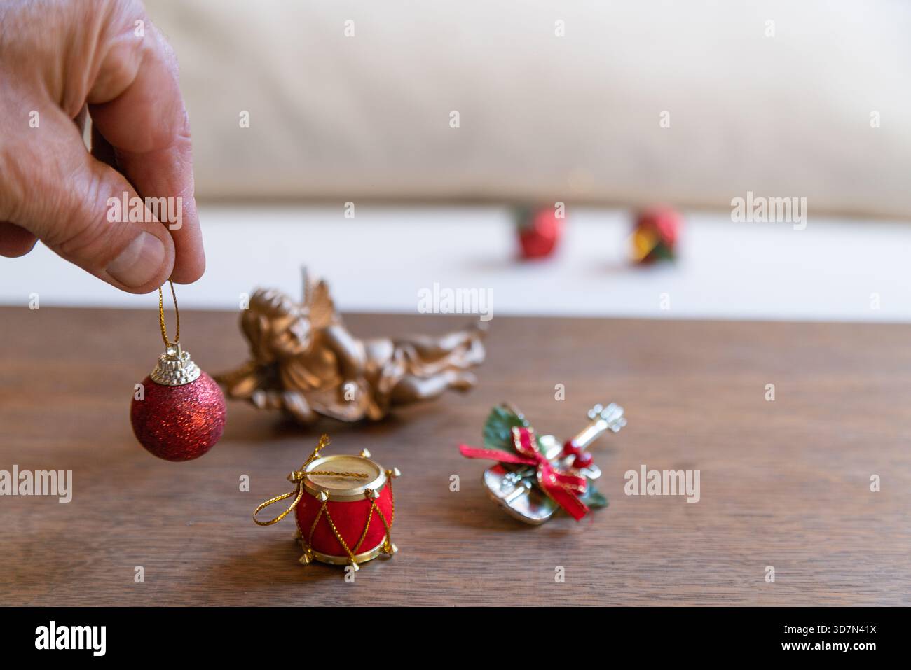 Hand hält eine rote glitzernde weihnachtskugel über anderen festlichen Ornamenten auf einem Holztisch Stockfoto