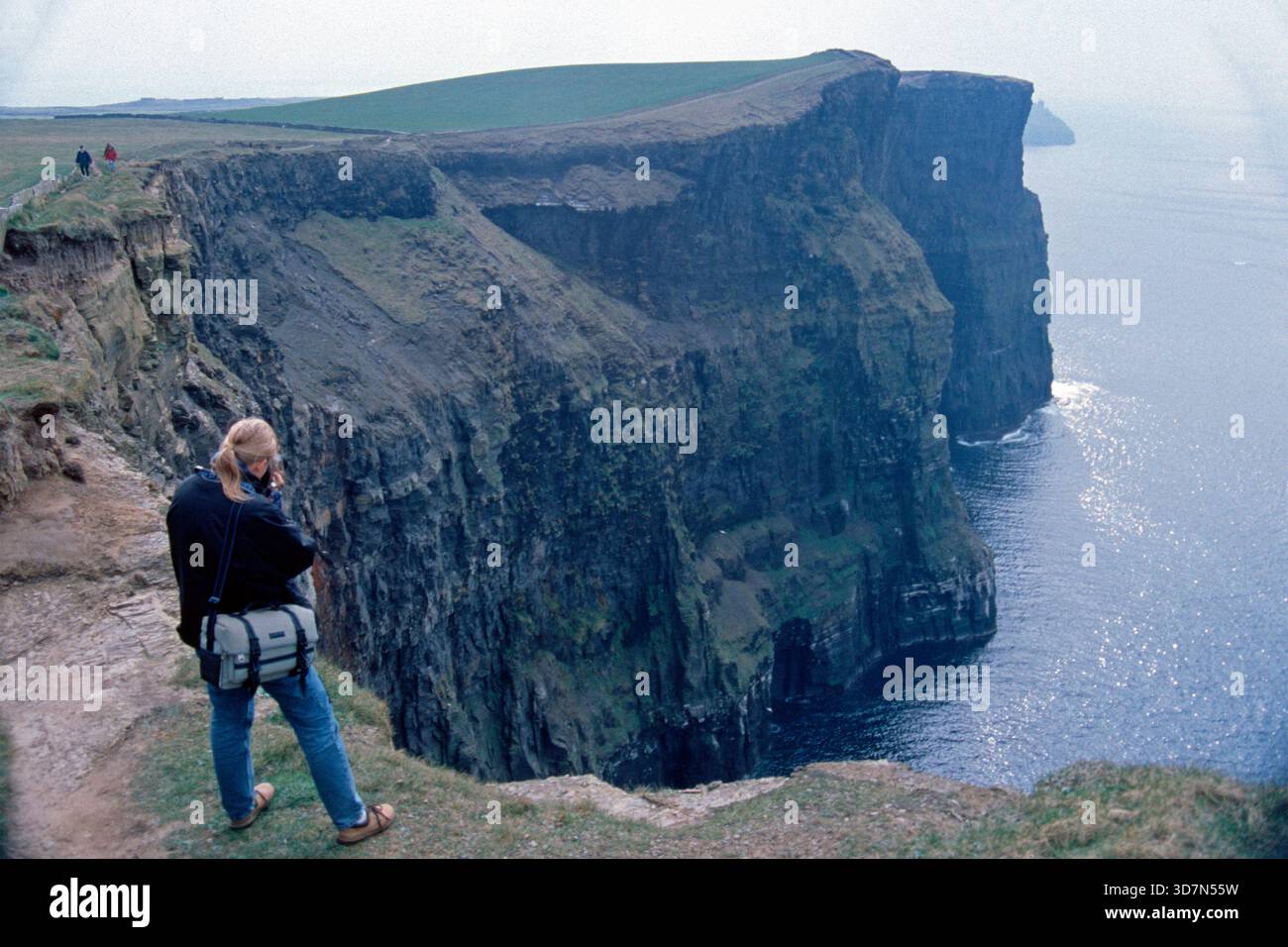 Junge Frau, die Fotos am Rande der Klippen macht, es gab noch keinen Zaun, Cliffs of Moher, County Clare, Republik Irland, April 1996 Stockfoto