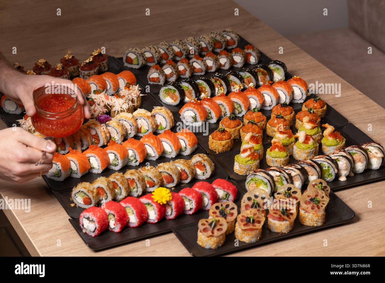 Eine Person arrangiert eine große Gourmet-Platte mit verschiedenen Sushi- und Maki-Brötchen, einschließlich Optionen mit Lachs, rotem Kaviar und raffinierten Belägen, in einem Re Stockfoto
