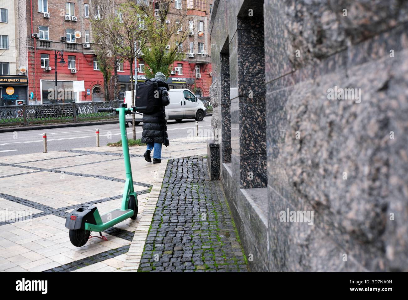 Im Frühjahr läuft eine Person an einem geparkten Elektroroller auf einem Bürgersteig der Stadt vorbei. Kiew, Ukraine, 26. November 2025. Stockfoto