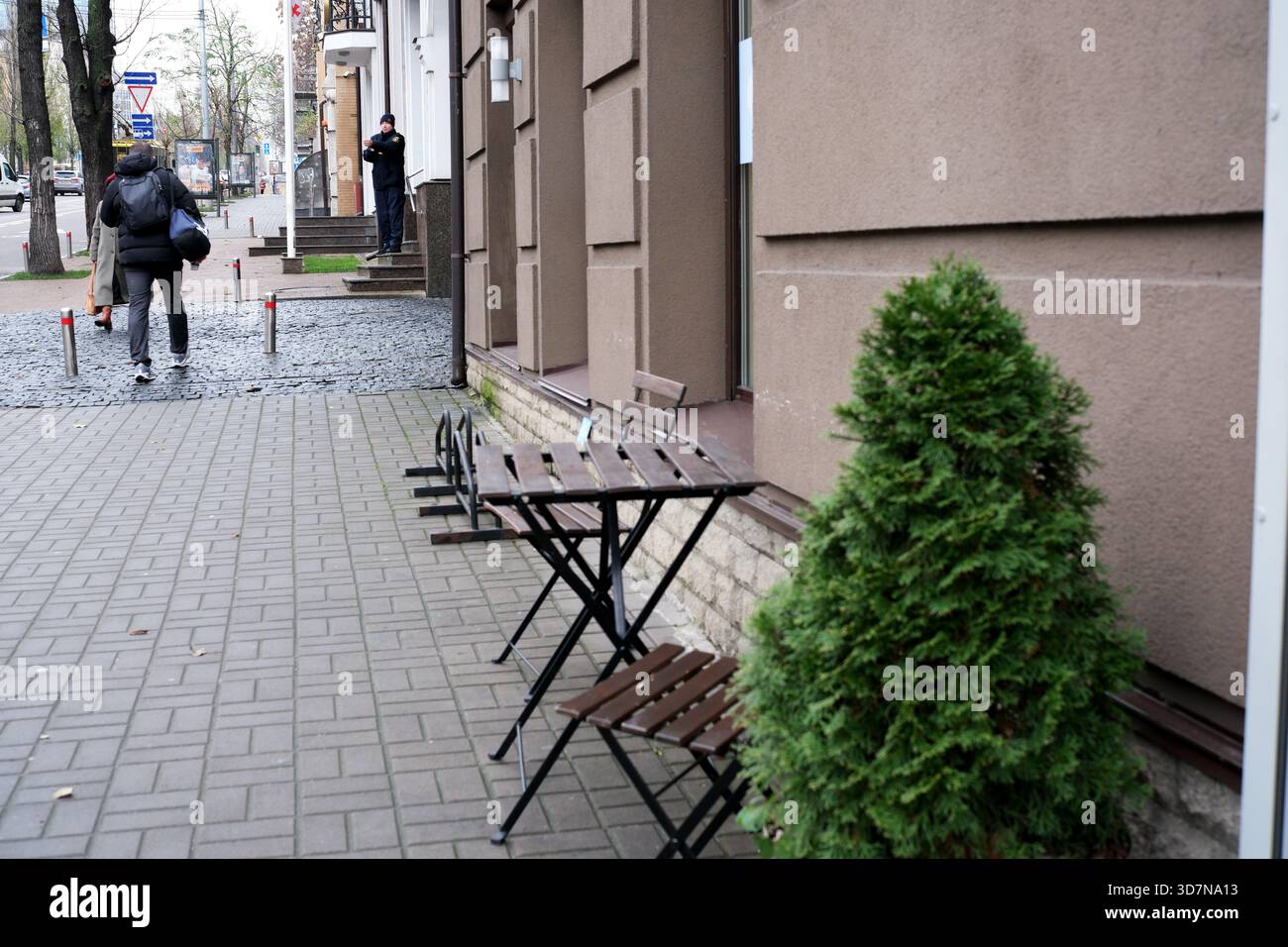 Kleine Holztische säumen den Bürgersteig neben einem grünen Sträucher und laden zum Entspannen ein. Kiew, Ukraine, 26. November 2025. Stockfoto