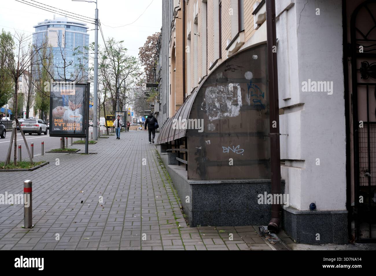 Die Leute schlendern auf einem belebten Bürgersteig, umgeben von Stadtarchitektur. Kiew, Ukraine, 26. November 2025. Stockfoto