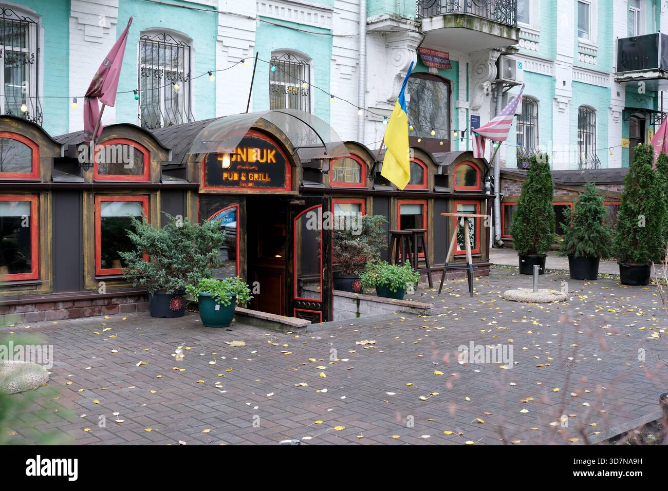 Ein gemütlicher Pub und Grill mit bunten Fahnen hebt sich an einem bewölkten Herbsttag hervor. Kiew, Ukraine, 26. November 2025. Stockfoto