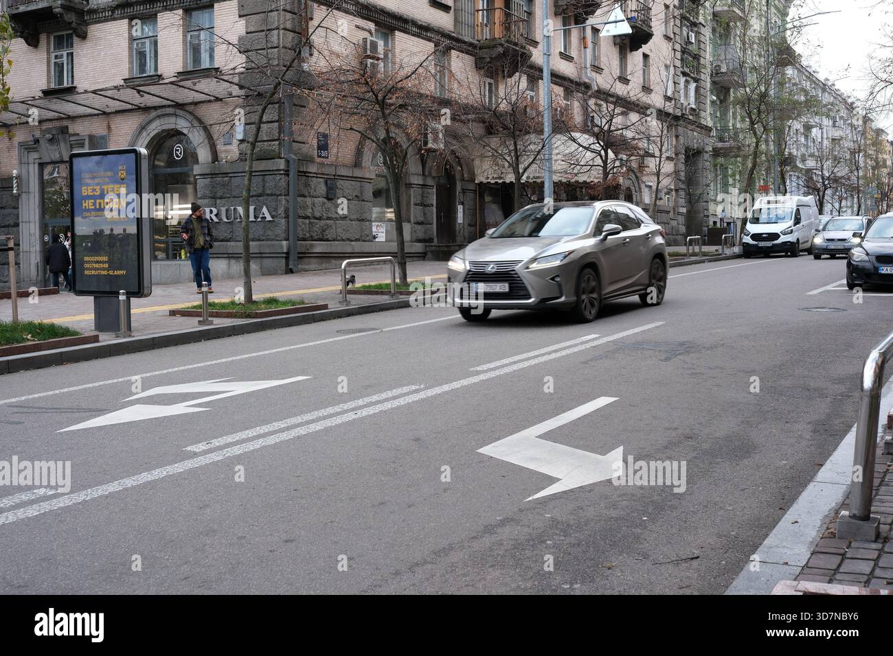 Ein elegantes Auto fährt eine ruhige Stadtstraße entlang, während die Leute in der Nähe laufen. Kiew, Ukraine. November 2025. Stockfoto