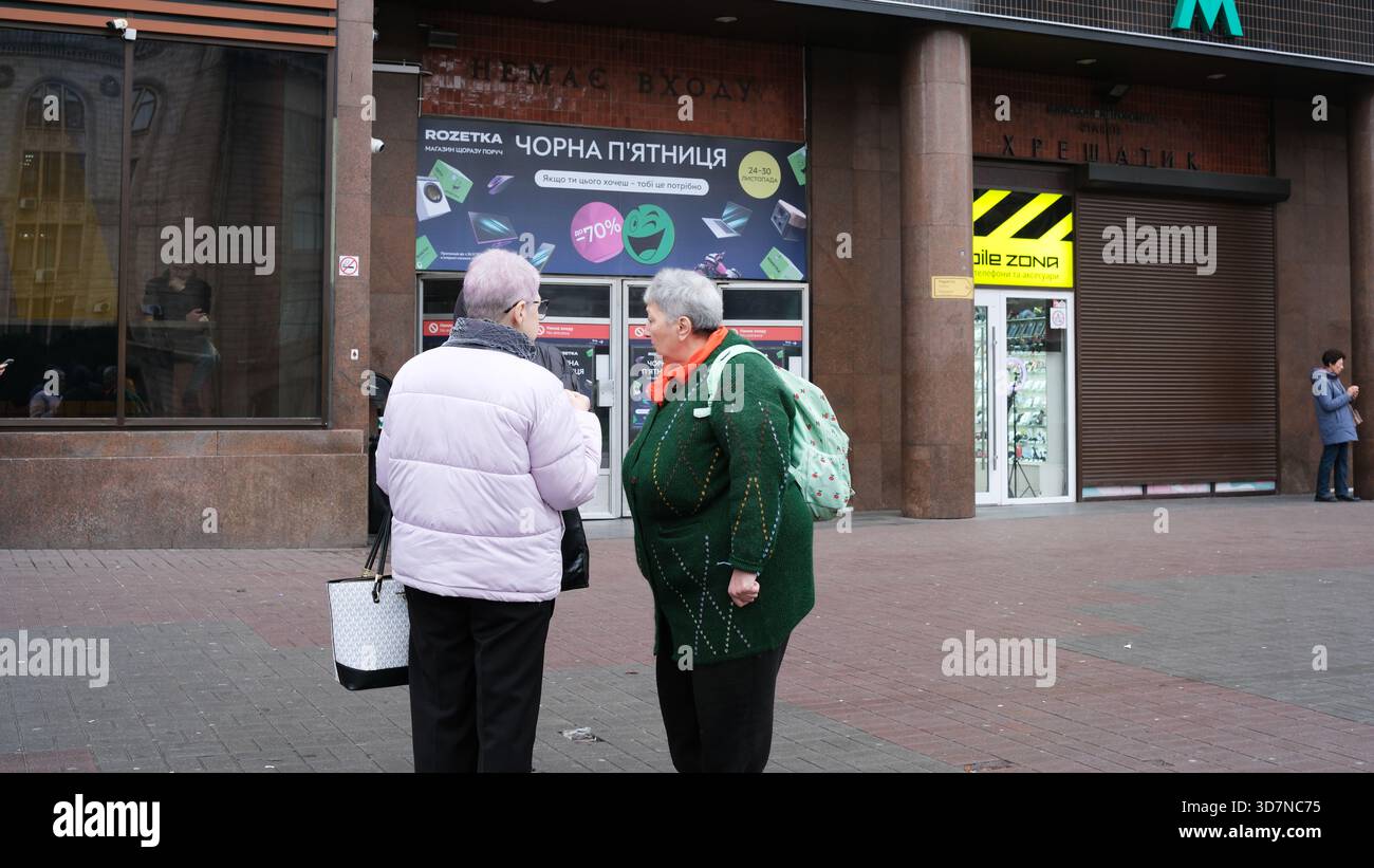 Zwei ältere Frauen unterhalten sich während des Winters vor einem Geschäft in einem belebten Stadtgebiet. Chreshtschatjk, Kiew, Ukraine. November 2025. Stockfoto