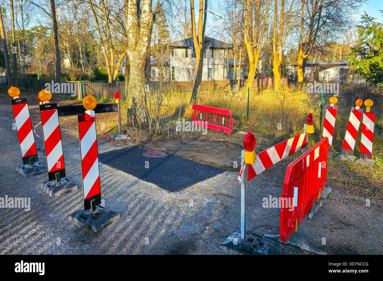Helle Warnschranken und Lichter umgeben einen frisch geflickten Straßenabschnitt in einem Wohngebiet, was auf kürzlich durchgeführte Reparaturarbeiten und eingeschränkte Zugangsmöglichkeiten hinweist Stockfoto
