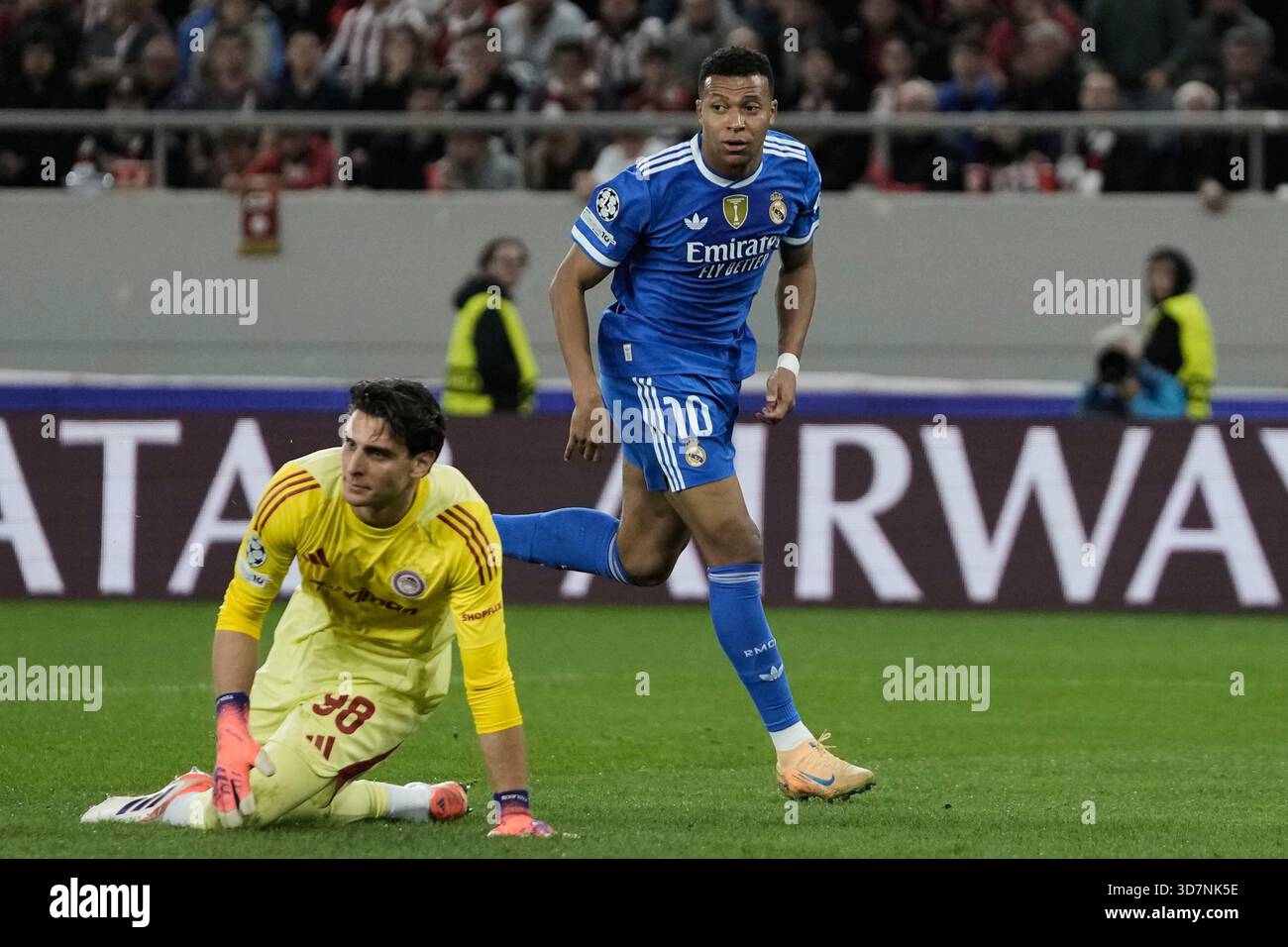 Real Madrid's Kylian Mbappe, top, goes for the ball past Olympiacos' goalkeeper Konstantinos Tzolakis after scoring his side's opening goal during the Champions League opening phase soccer match between Olympiacos and Real Madrid in Piraeus port, near Athens, Greece, Wednesday, Nov. 26, 2025. (AP Photo/Thanassis Stavrakis) Stockfoto
