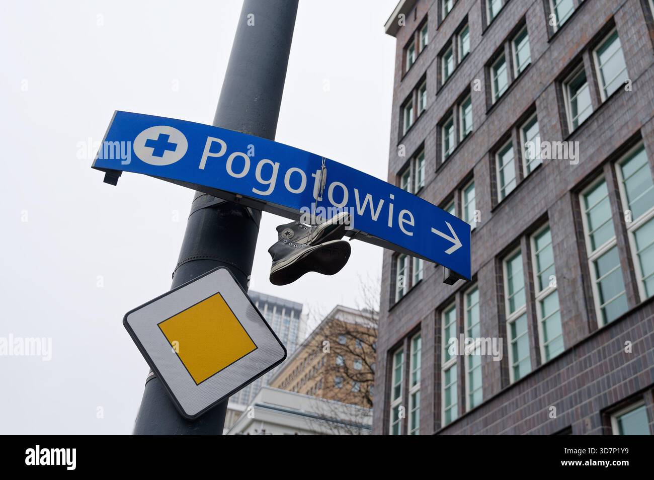 Blaues Pogotowie-Notfallschild an einem Straßenmast der Stadt mit einem Paar hängenden Sneakers. Stockfoto
