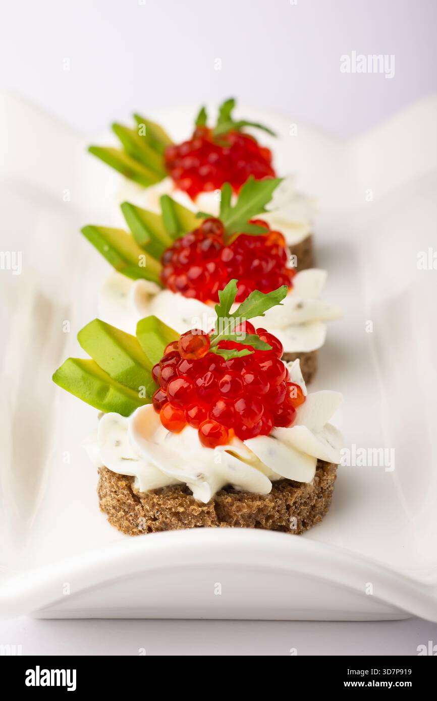Bunte Vorspeisen aus Roggenbrot werden auf einer weißen Platte präsentiert. Jedes Stück wird mit Sahne, Kaviar und frischen Gemüsescheiben garniert, perfekt für einen Stockfoto