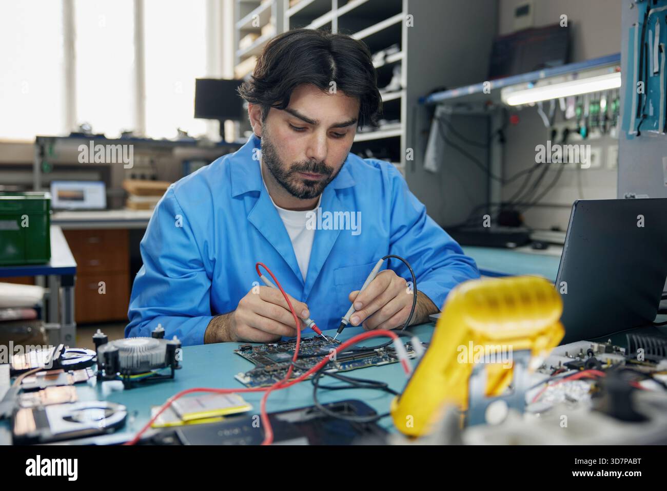Ein Arbeiter, der in einem blauen Mantel gekleidet ist, konzentriert sich auf die Arbeit mit einem Motherboard Stockfoto
