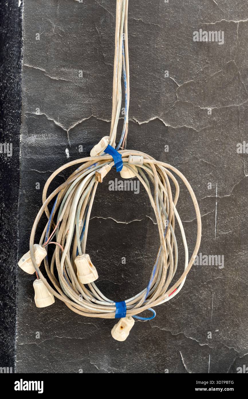Bündel teilweise beschädigter Verlängerungskabel mit freiliegenden Steckern und verwickelten Drähten. Stockfoto
