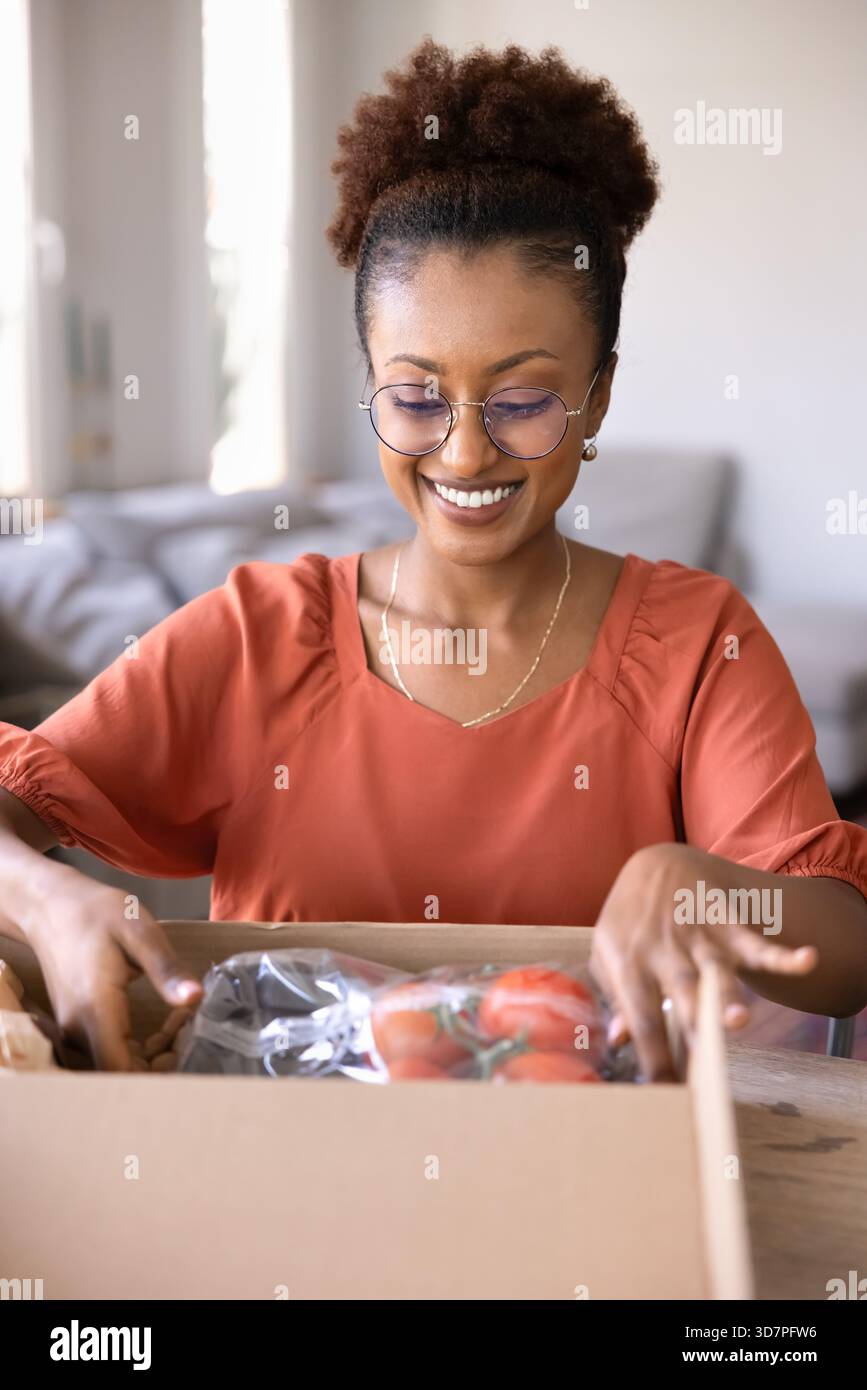 Glückliche junge afroamerikanische Supermarktkundschaft, die den Karton auspackt Stockfoto